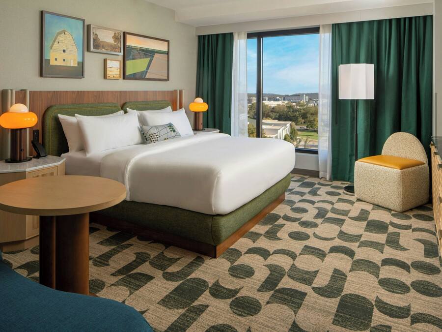 Habitación de hotel con una cama grande, una mesa redonda, una silla y vistas al exterior.