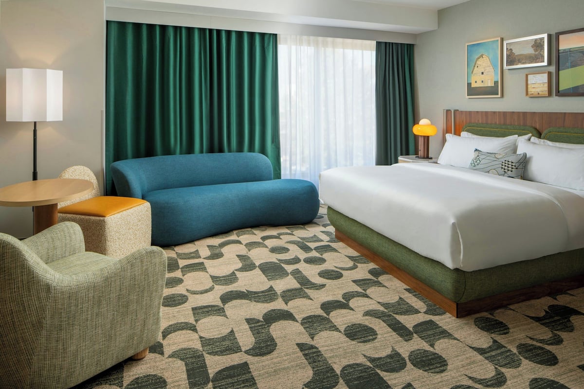 A hotel room with a bed, a sofa, a chair, a lamp, and a window with curtains.
