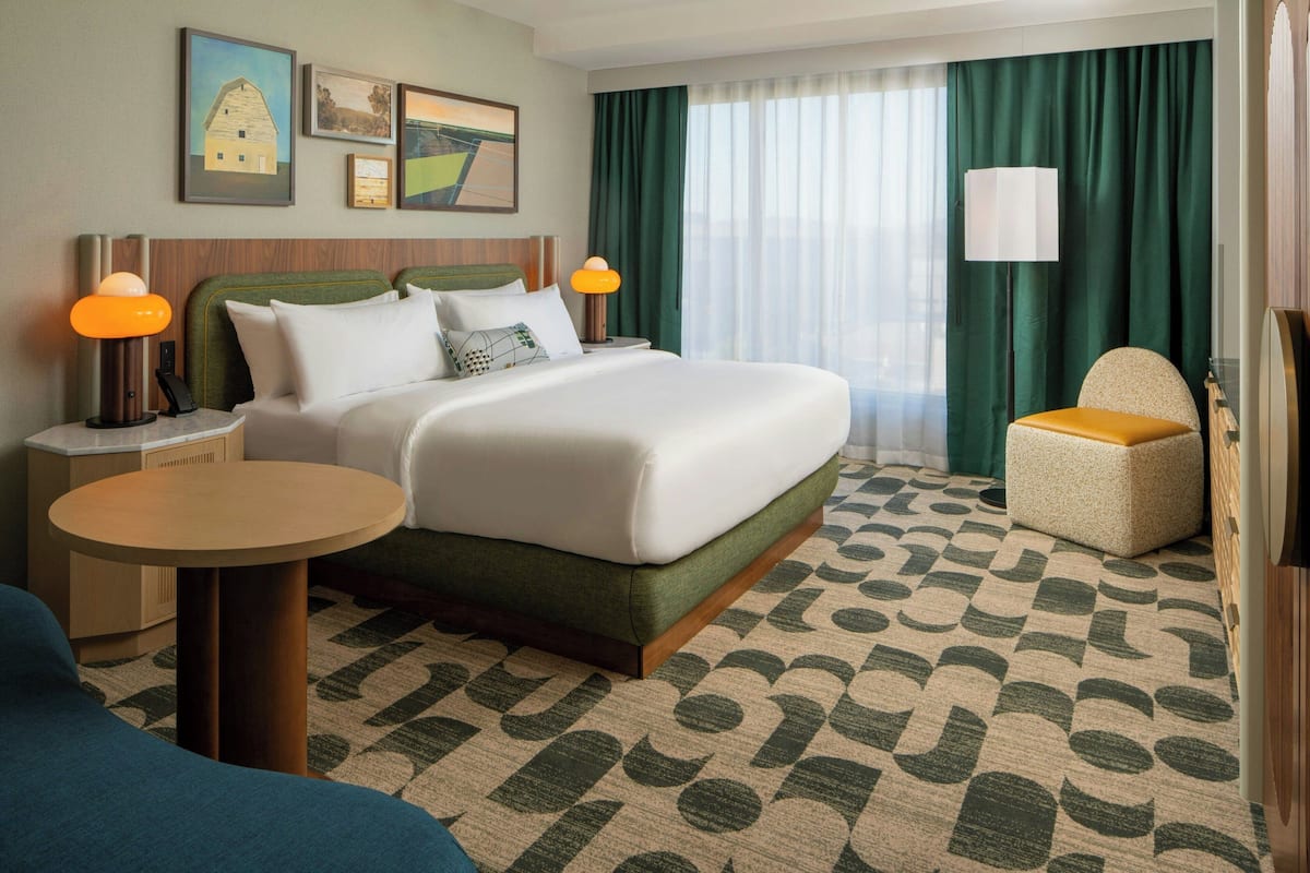 A hotel room with a bed, two bedside tables, a chair, a round table, and a patterned carpet.