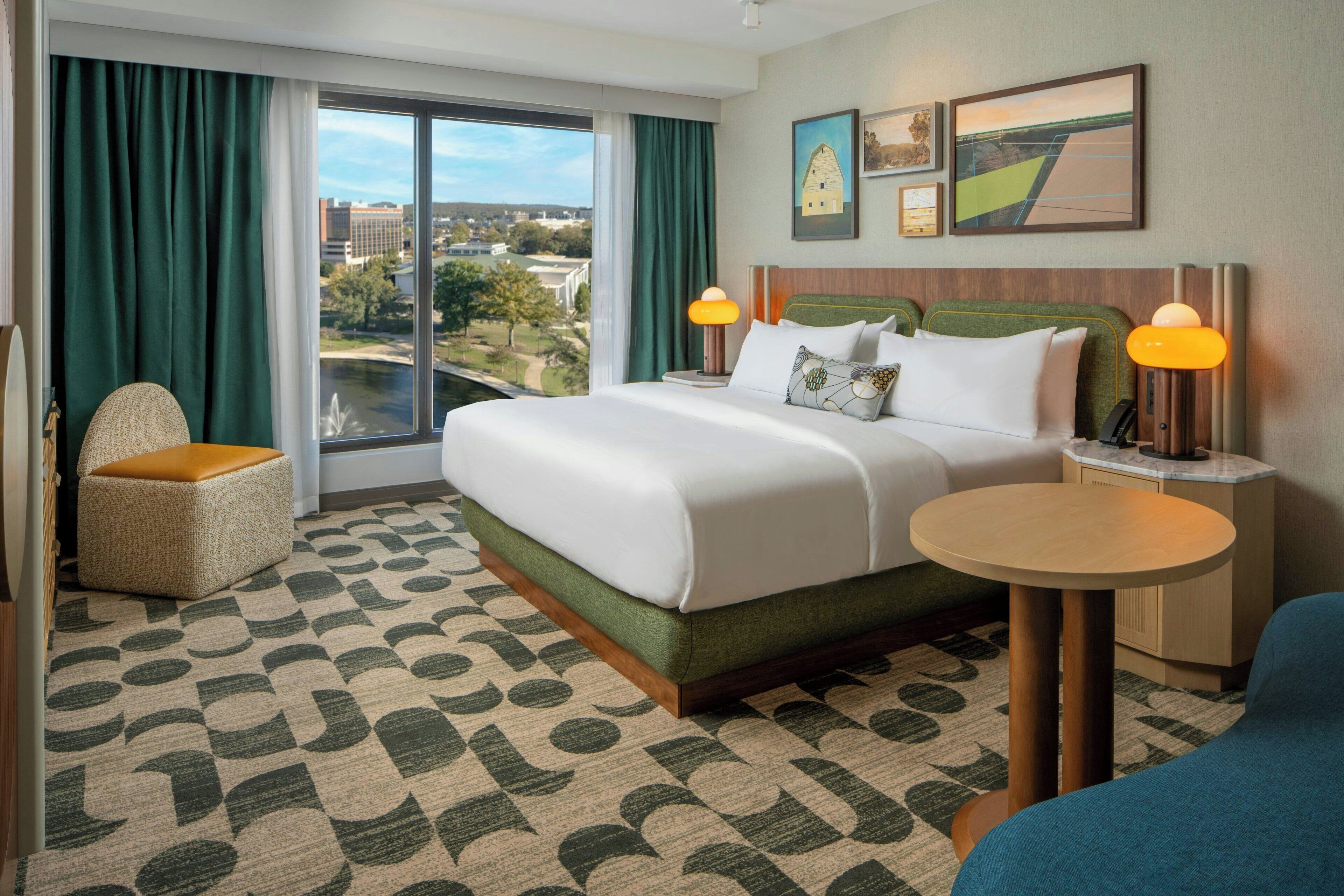 Une chambre d’hôtel avec un grand lit, une table ronde, une chaise et une vue sur la ville par la fenêtre.