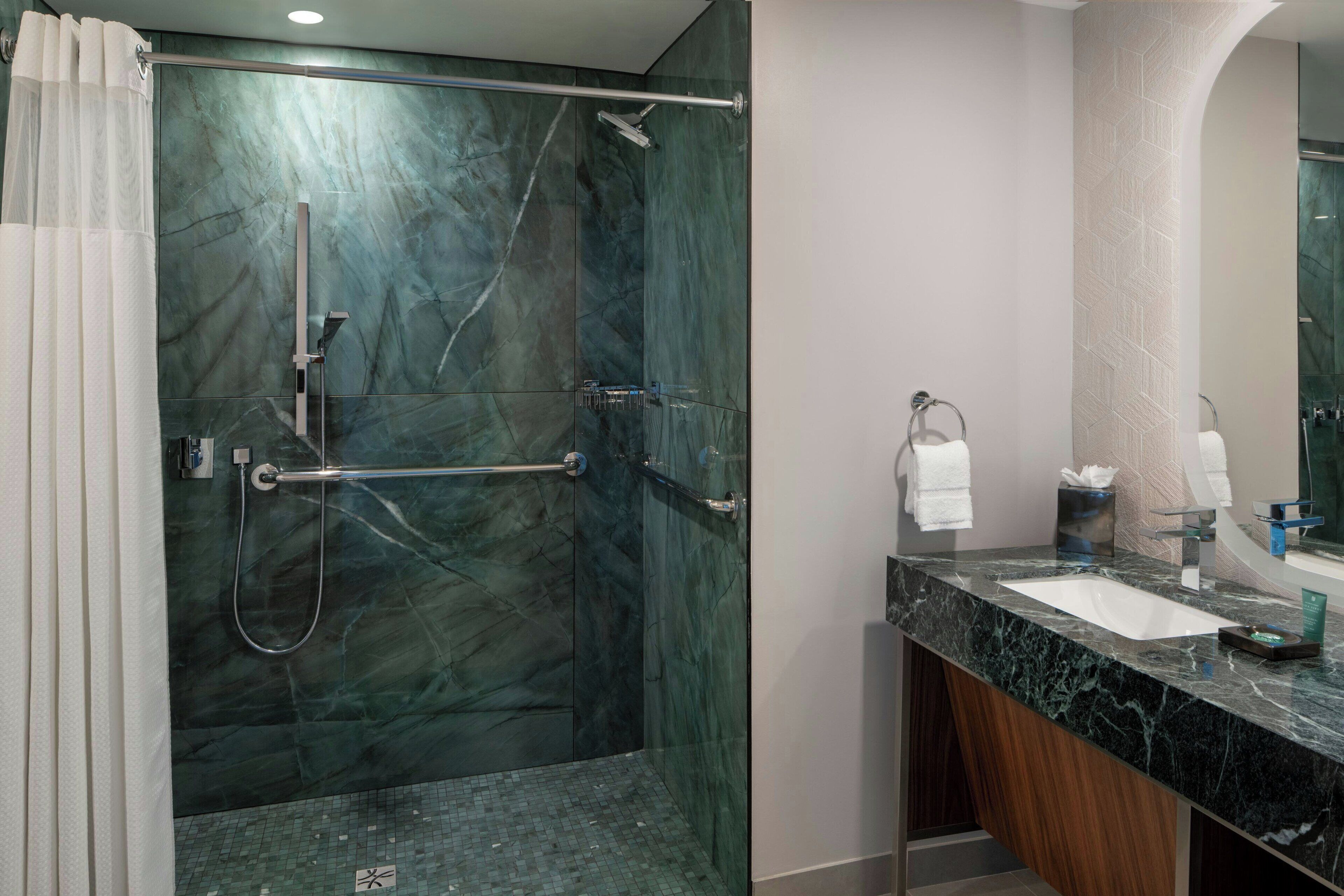 Une salle de bain moderne dotée d’une douche à parois de verre, d’un comptoir en marbre et d’un grand miroir.
