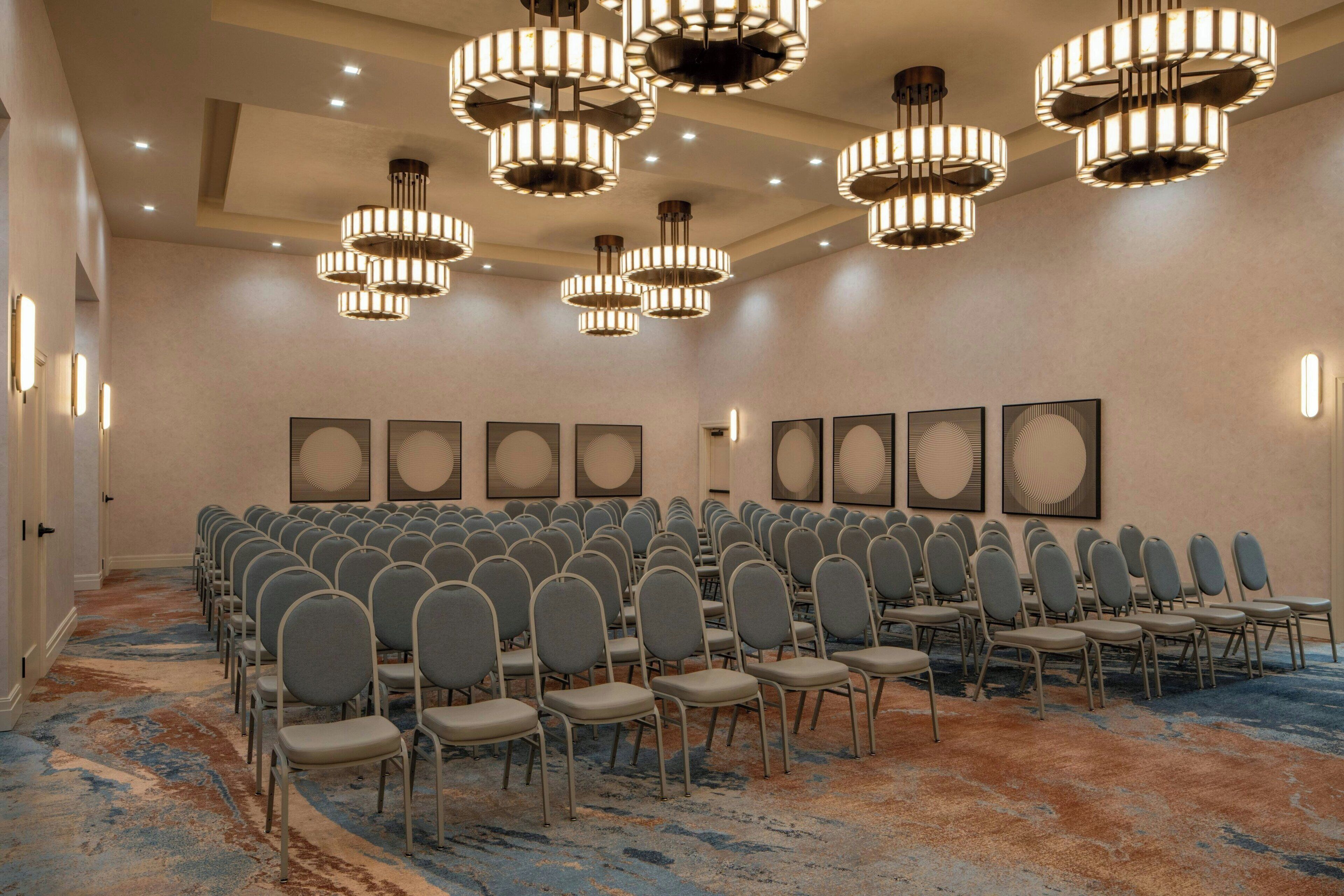 Un salón de conferencias con filas de sillas, varios candelabros y obras de arte enmarcadas en las paredes.