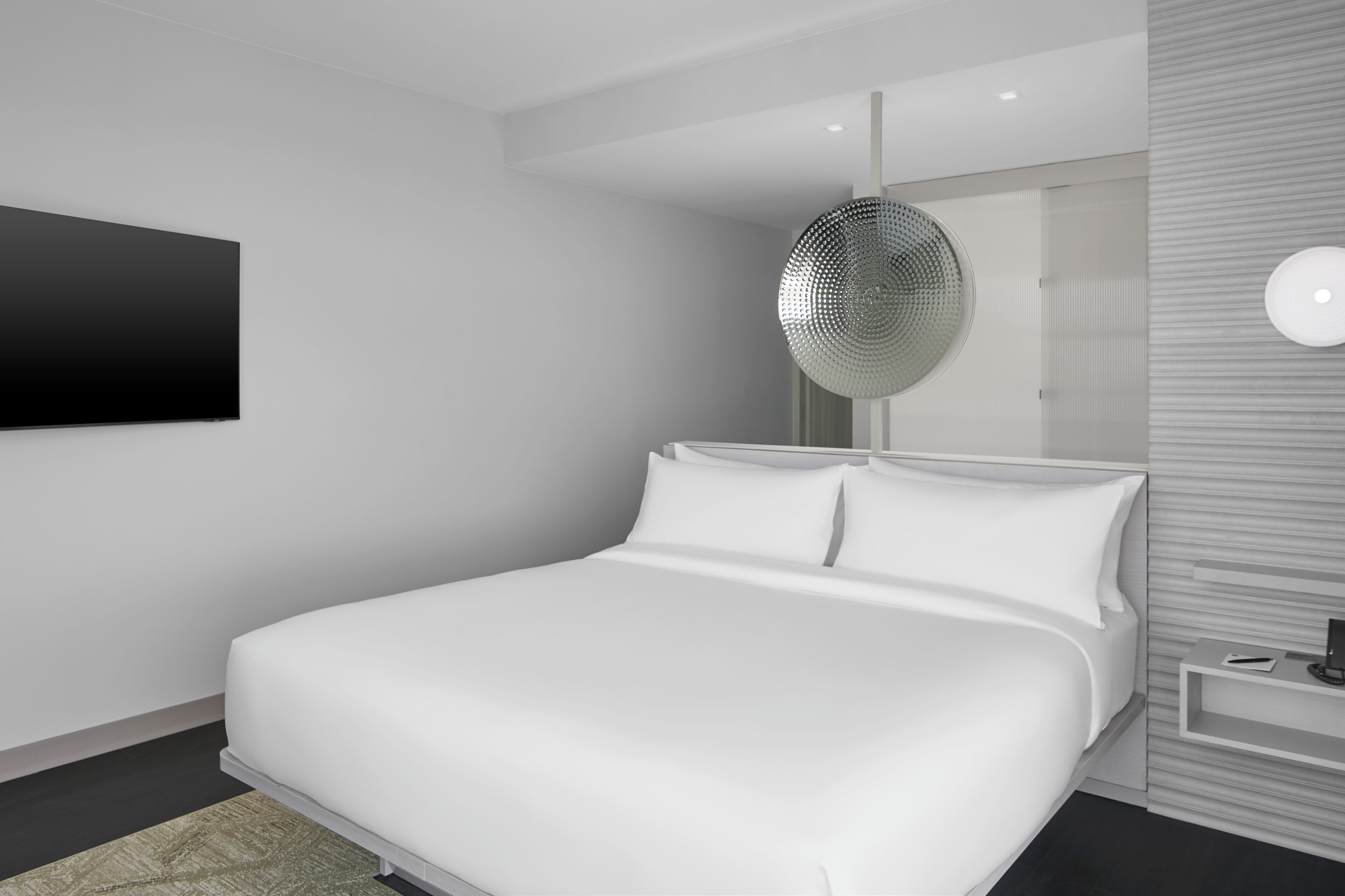 A modern bedroom with a large bed, a wall-mounted TV, a decorative mirror, and a bedside table with a lamp.