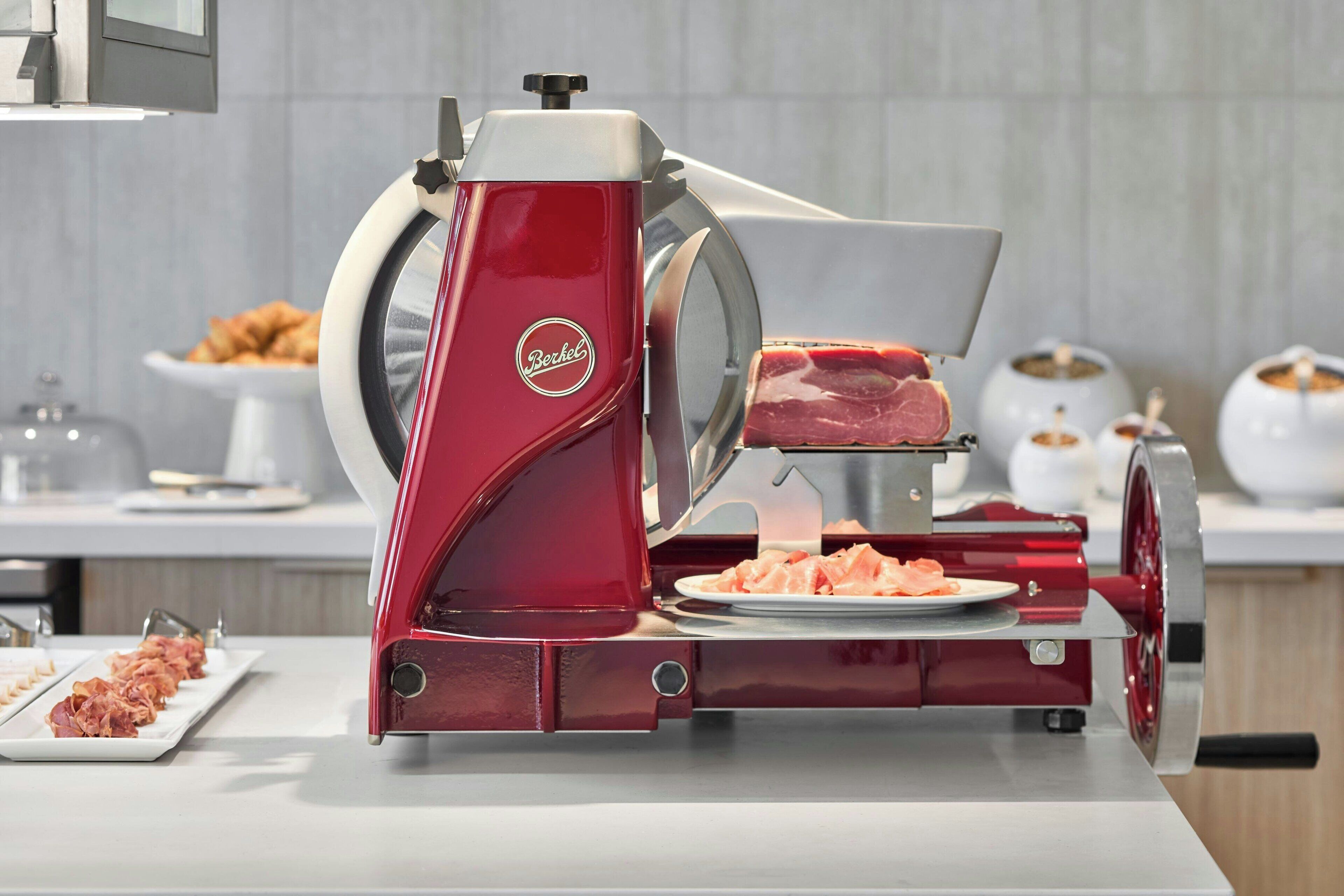 A red meat slicer with a plate of sliced meat and a plate of raw meat.