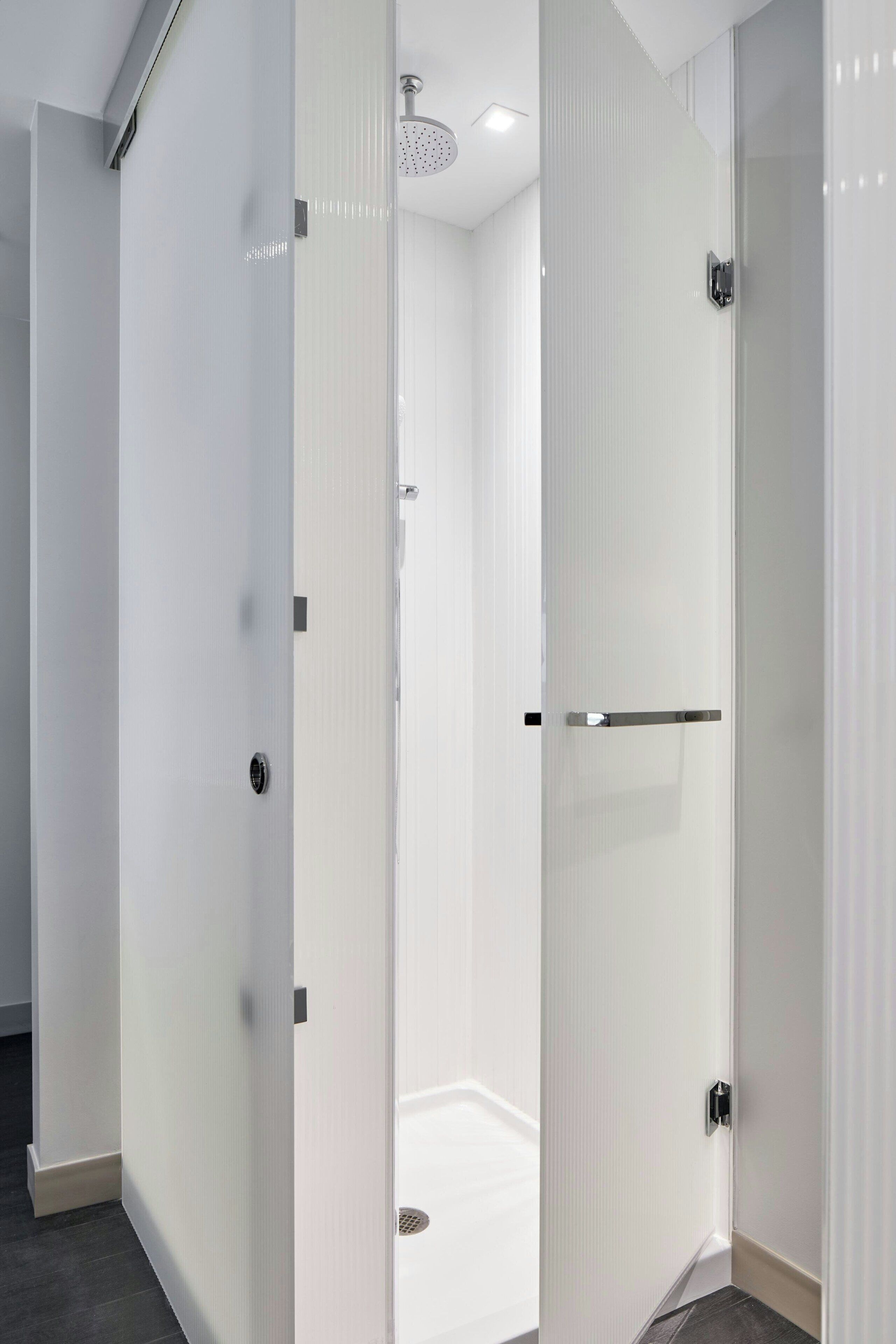 A modern bathroom with a glass shower enclosure, white walls, and a visible showerhead.