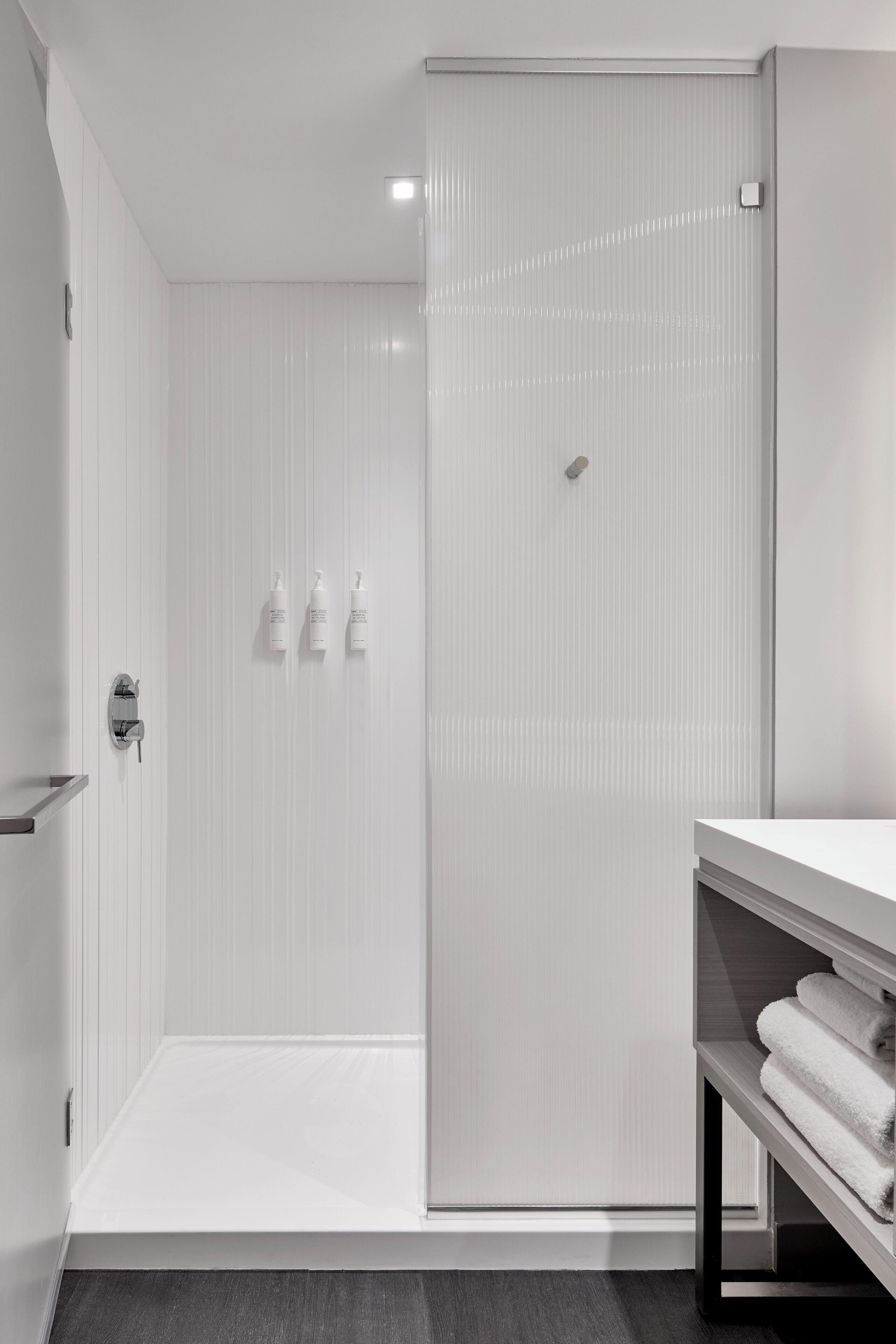 Une salle de bain moderne avec une douche à l’italienne, un meuble-lavabo blanc doté d’un porte-serviettes et une porte de douche en verre.