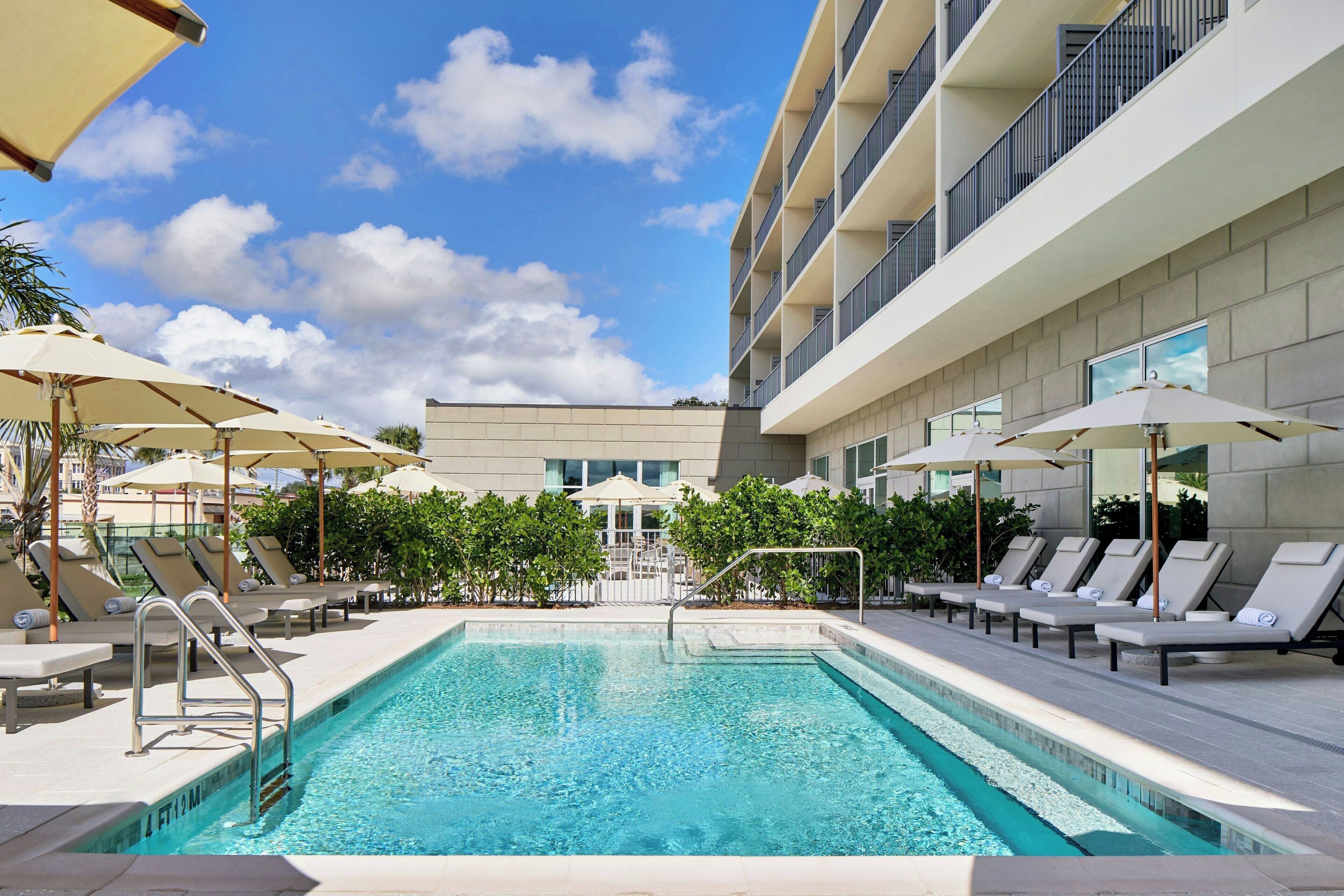 Une piscine entourée de chaises longues et de parasols, le tout bordé par un immeuble doté de nombreux balcons.