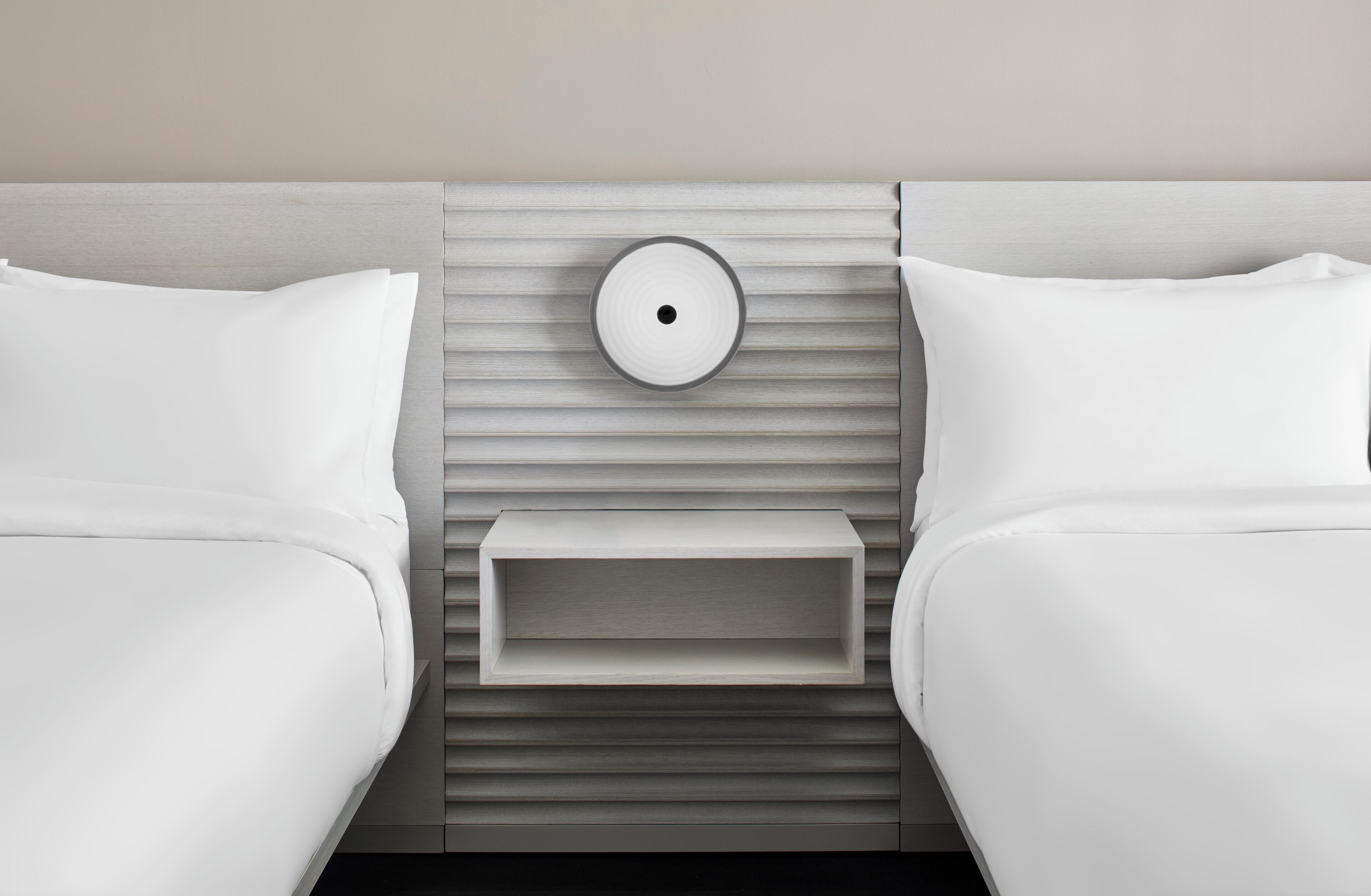 A modern hotel room with two beds, a bedside table, and a wall-mounted light fixture.