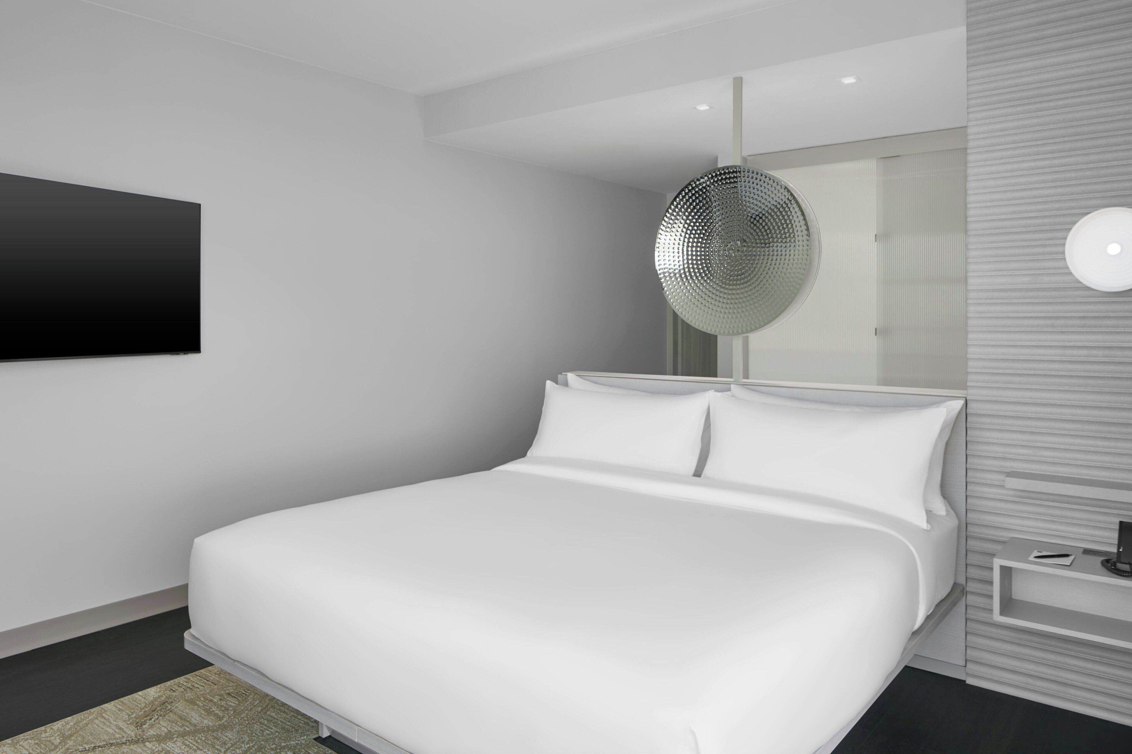 Ein modernes Schlafzimmer mit einem großen Bett, einem an der Wand montierten Fernseher und einem einzigartigen, runden Spiegel.