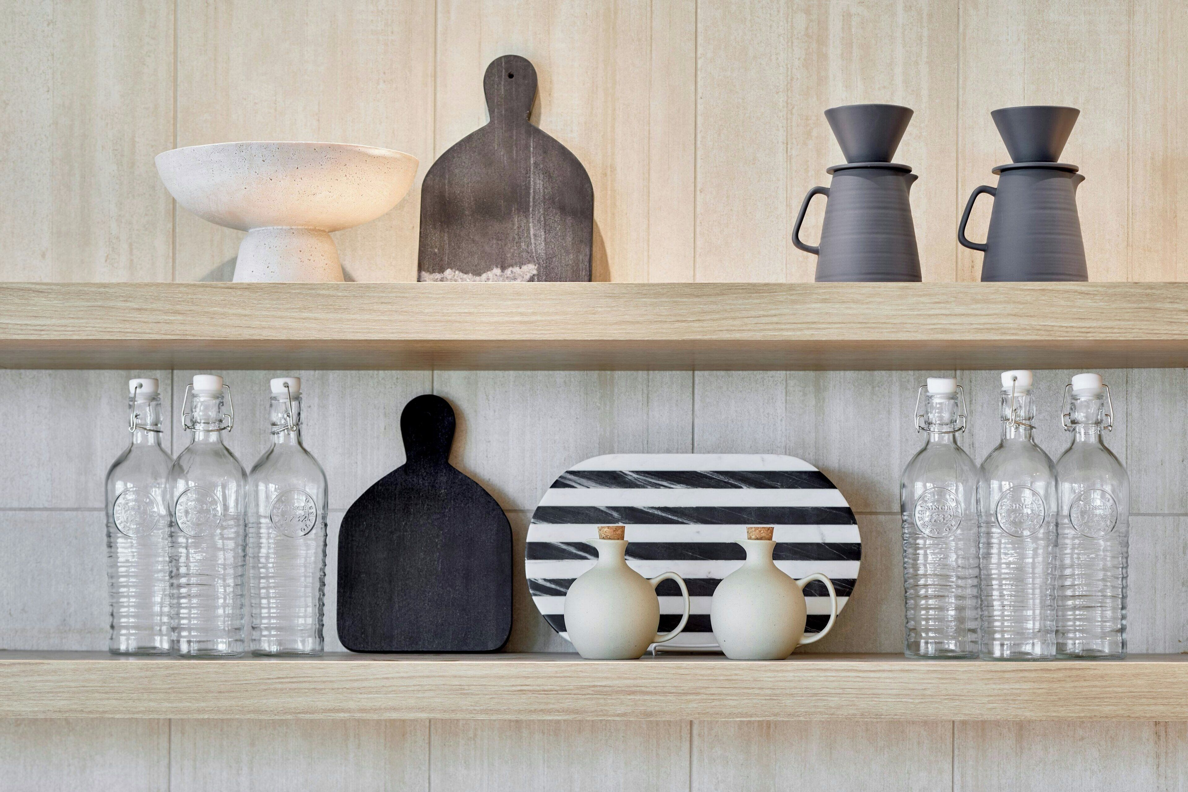 A shelf with various kitchen items including bottles, a cutting board, and decorative plates.