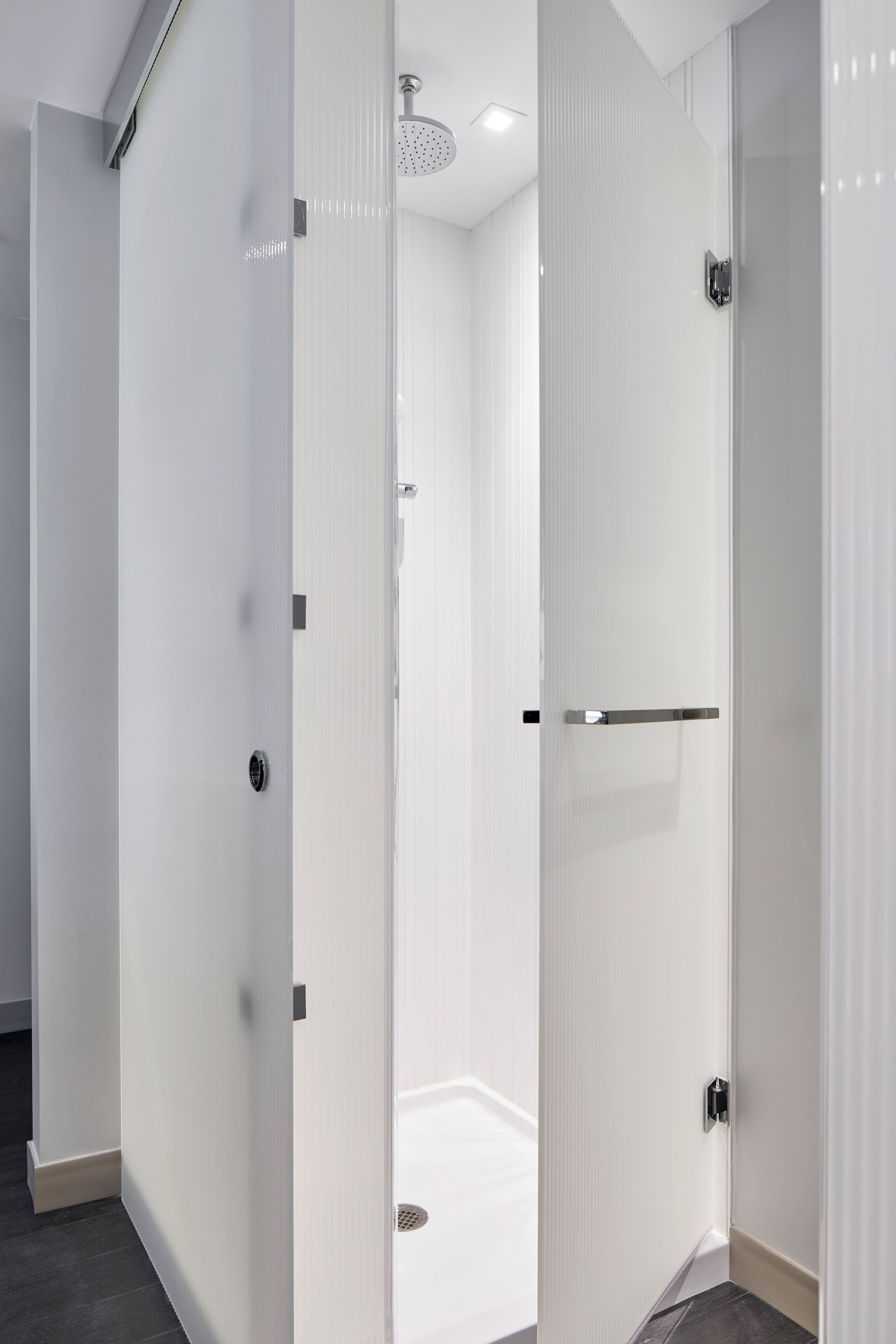 Une salle de bain moderne dotée d’une douche à parois de verre, d’un espace de douche carrelé de carreaux blancs et d’un pommeau de douche visible.