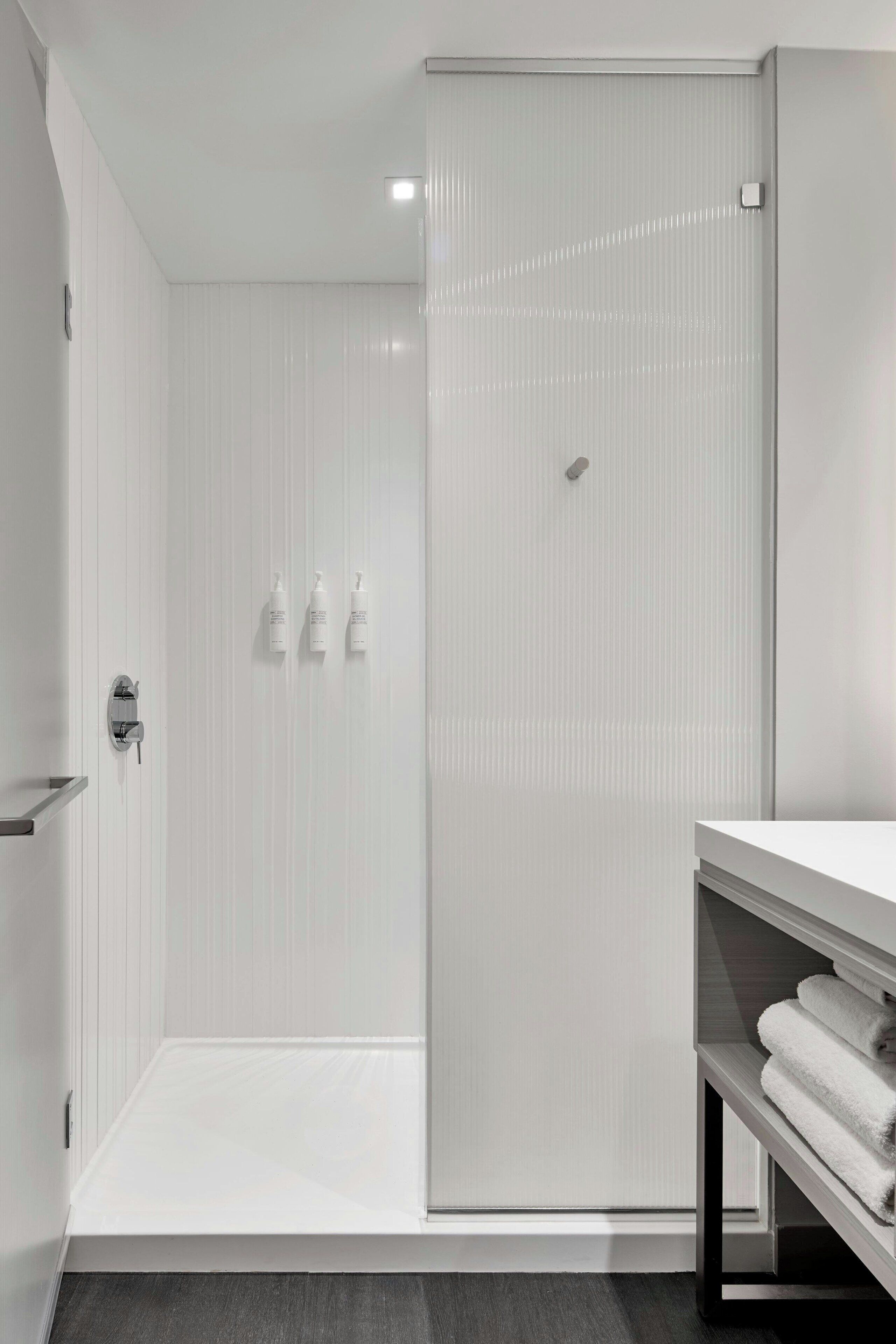 A modern bathroom with a shower, a toilet, and a sink. There are toiletries on the wall.