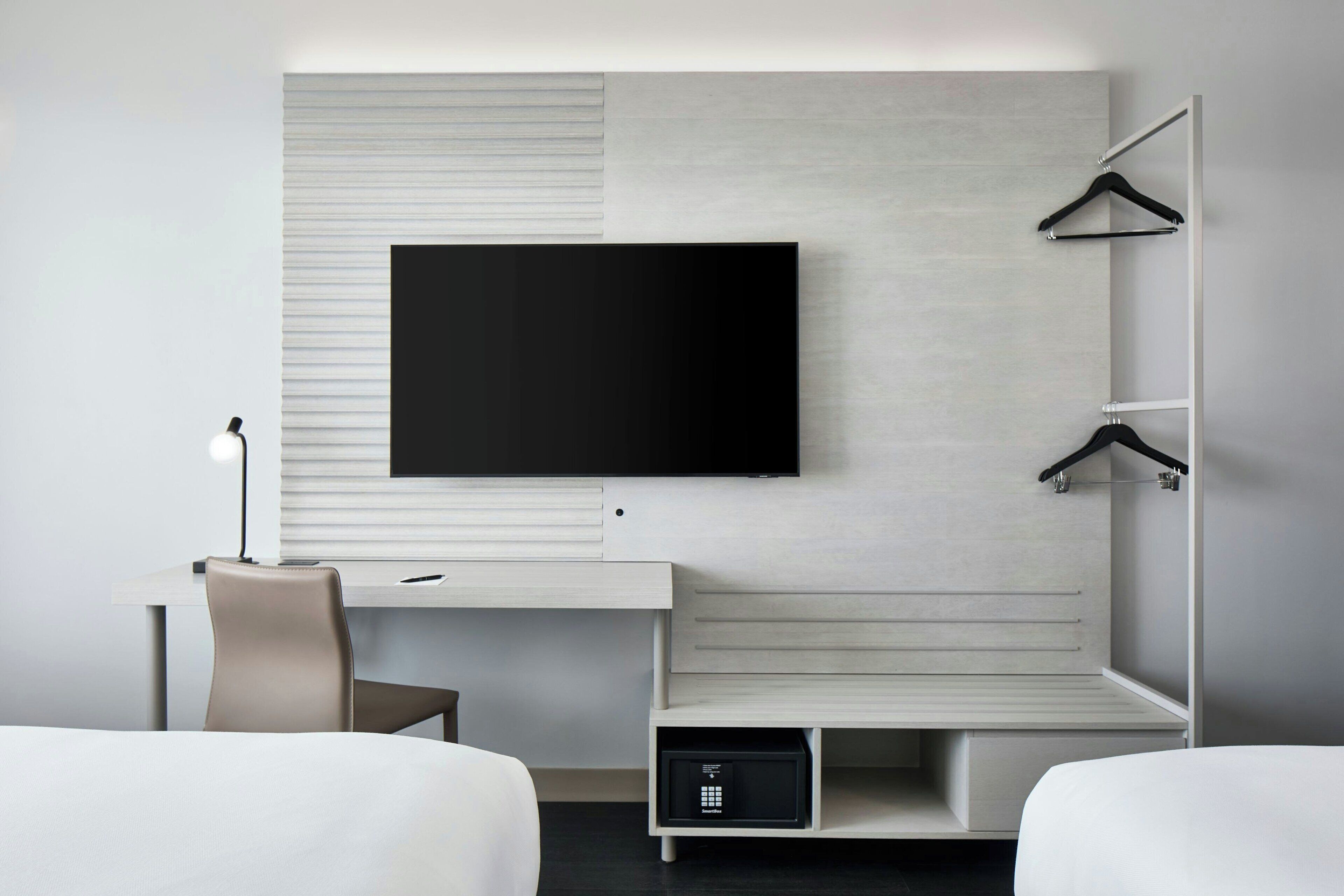 A modern hotel room with a flat-screen TV mounted on a wall, a desk with a chair, and a bed.