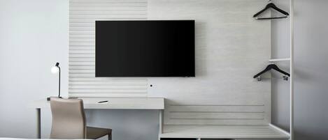 A modern hotel room with a flat-screen TV mounted on a wall, a desk with a chair, and a bed.