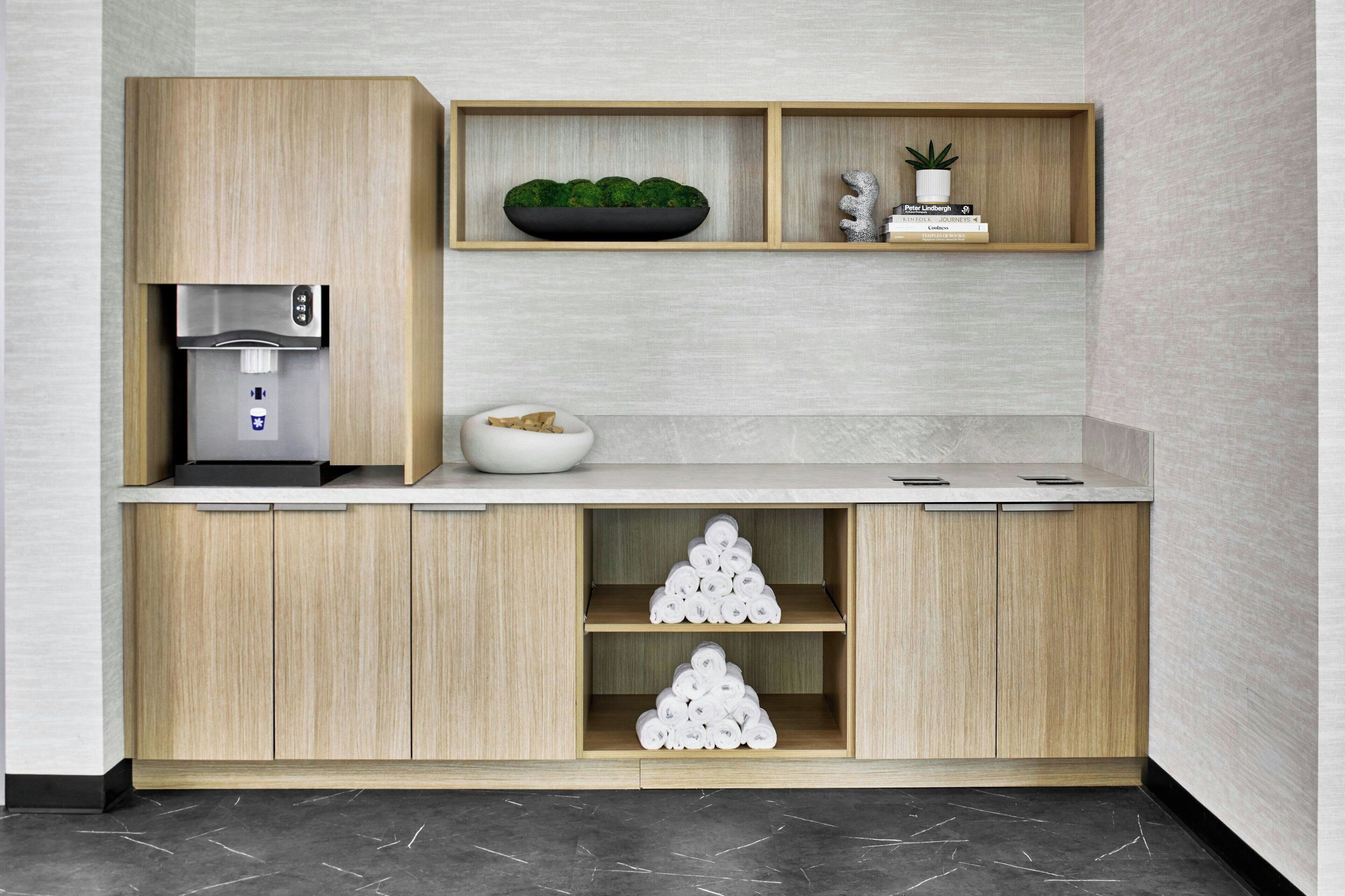Une cuisine moderne avec des meubles en bois, un appareil à café intégré, un saladier rempli de fruits et une étagère ornée d’objets décoratifs.