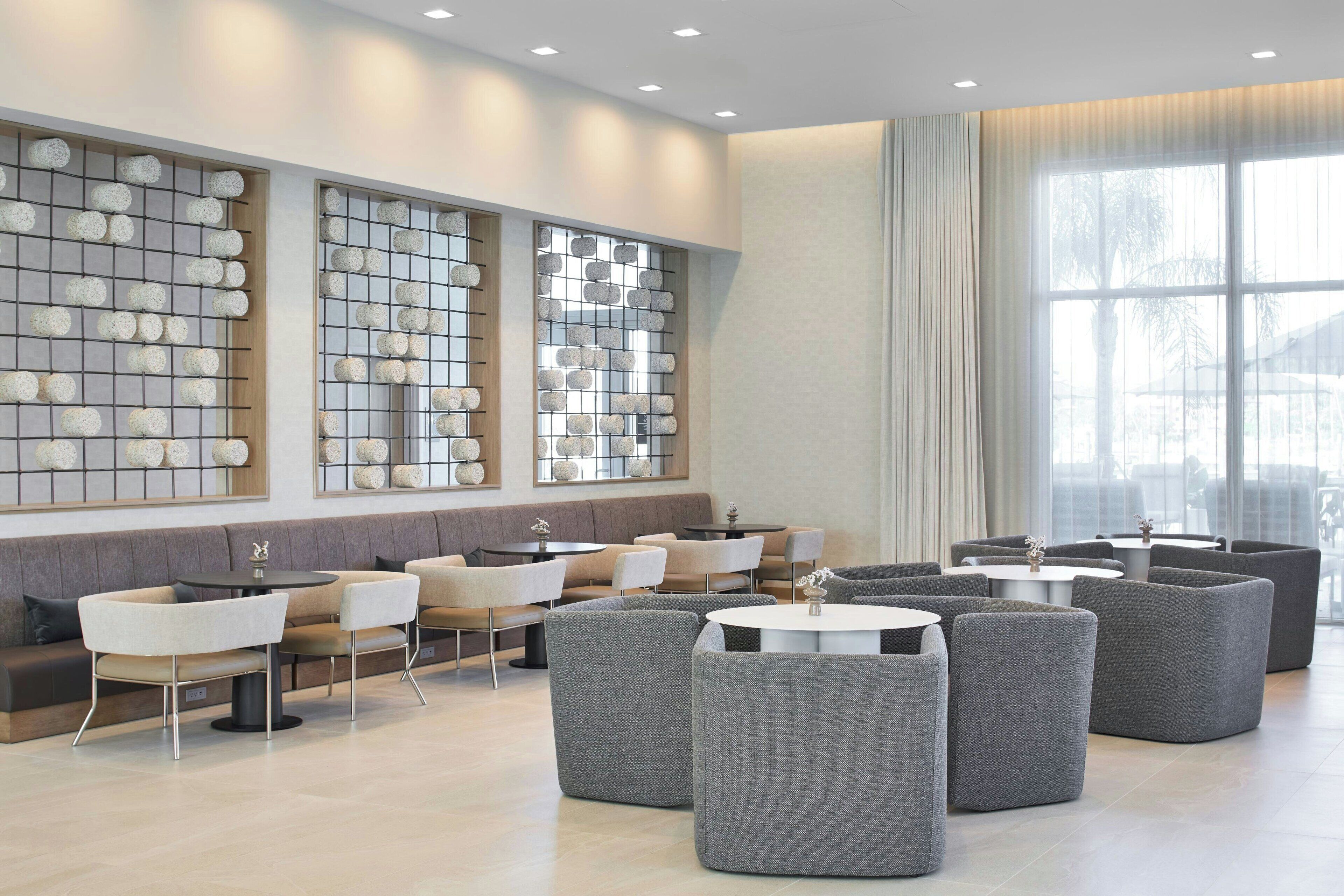 A modern lounge area with a long bench, multiple round tables, and grey upholstered chairs.