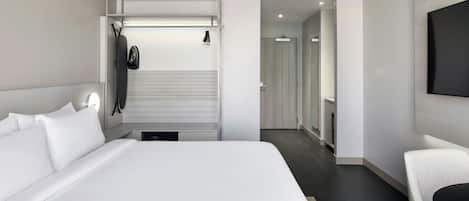 Moderni hotellihuone, jossa on suuri sänky, oleskelualue, televisio ja erillinen vaatehuone.