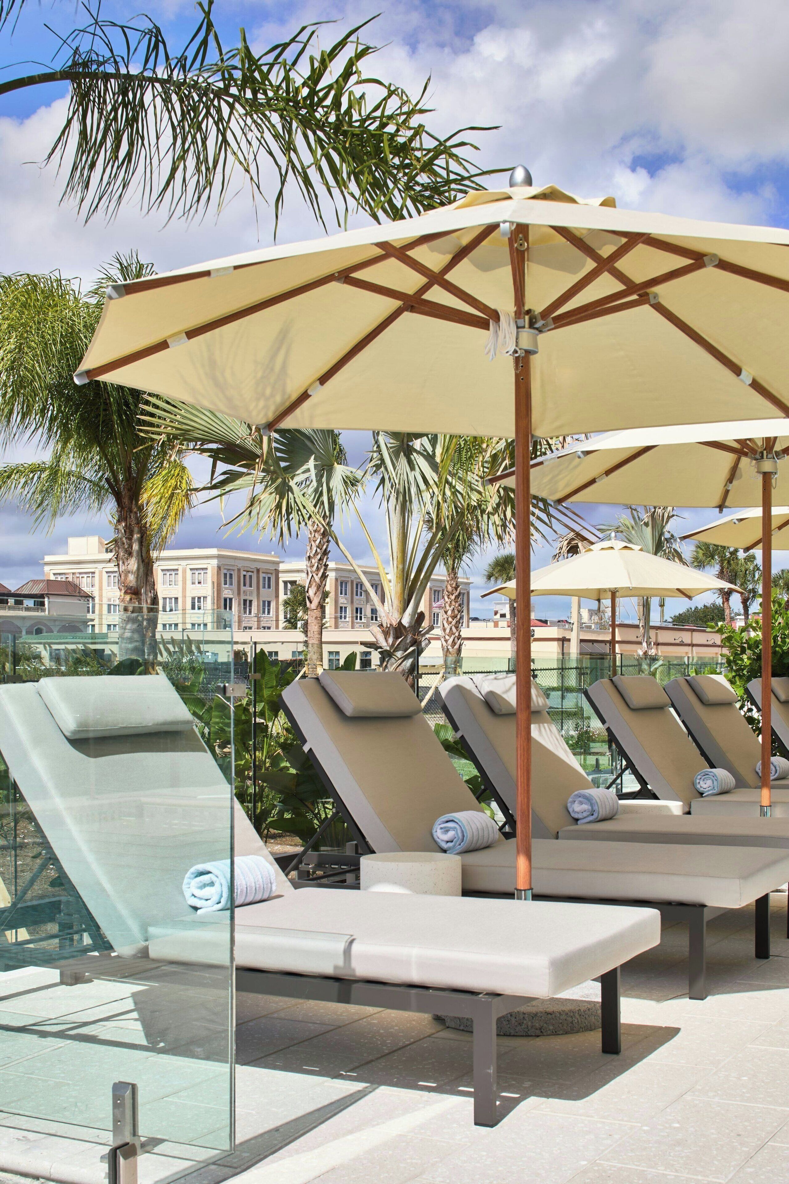 A poolside area with lounge chairs and umbrellas, a glass balustrade, and palm trees.