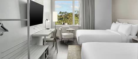A modern hotel room with a bed, a desk, a chair, a TV, and a window with a view of trees.