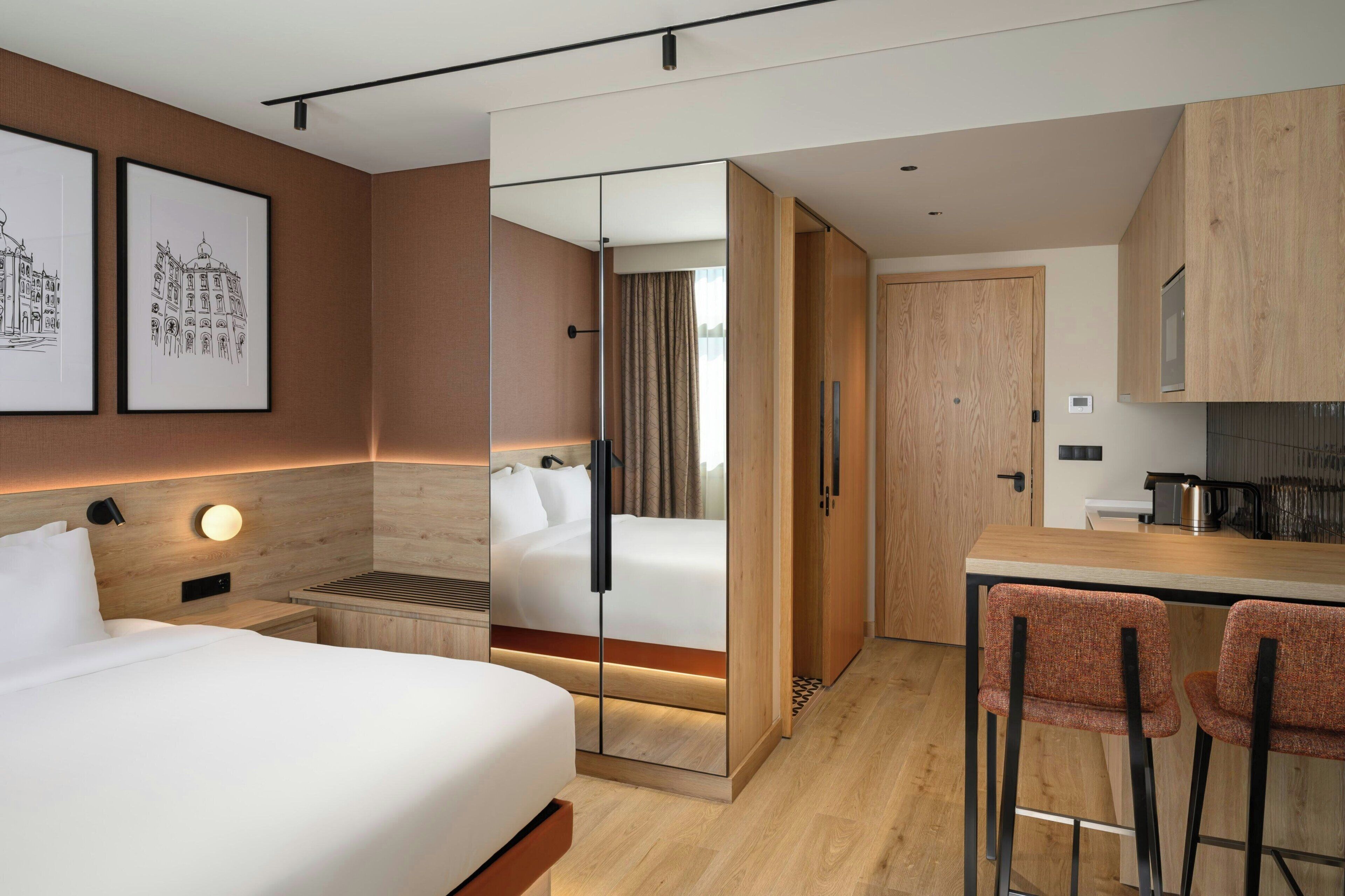 A modern hotel room with a bed, bedside table, and a desk area with two chairs.