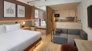 A modern hotel room with a large bed, a sofa, a small table, and a kitchen area with a microwave. - Residence Inn By Marriott Lisbon (Lisbon)