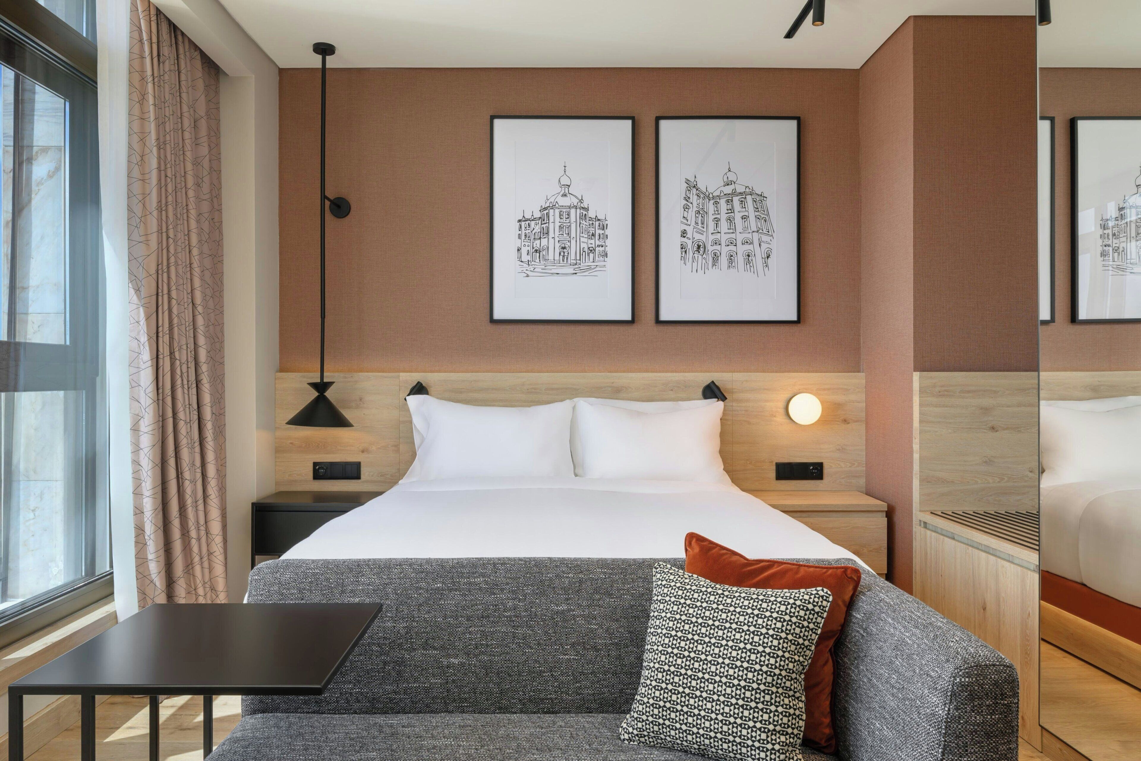 A hotel room with a bed, a nightstand, a table, a sofa, and two framed pictures on the wall.