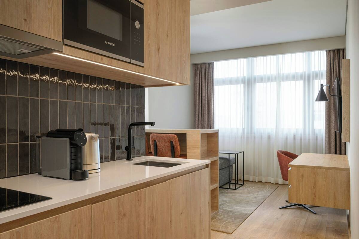 A modern kitchen with a Bosch microwave, a coffee maker, and a sink. There is a wooden cabinet above the counter and a chair in the background.