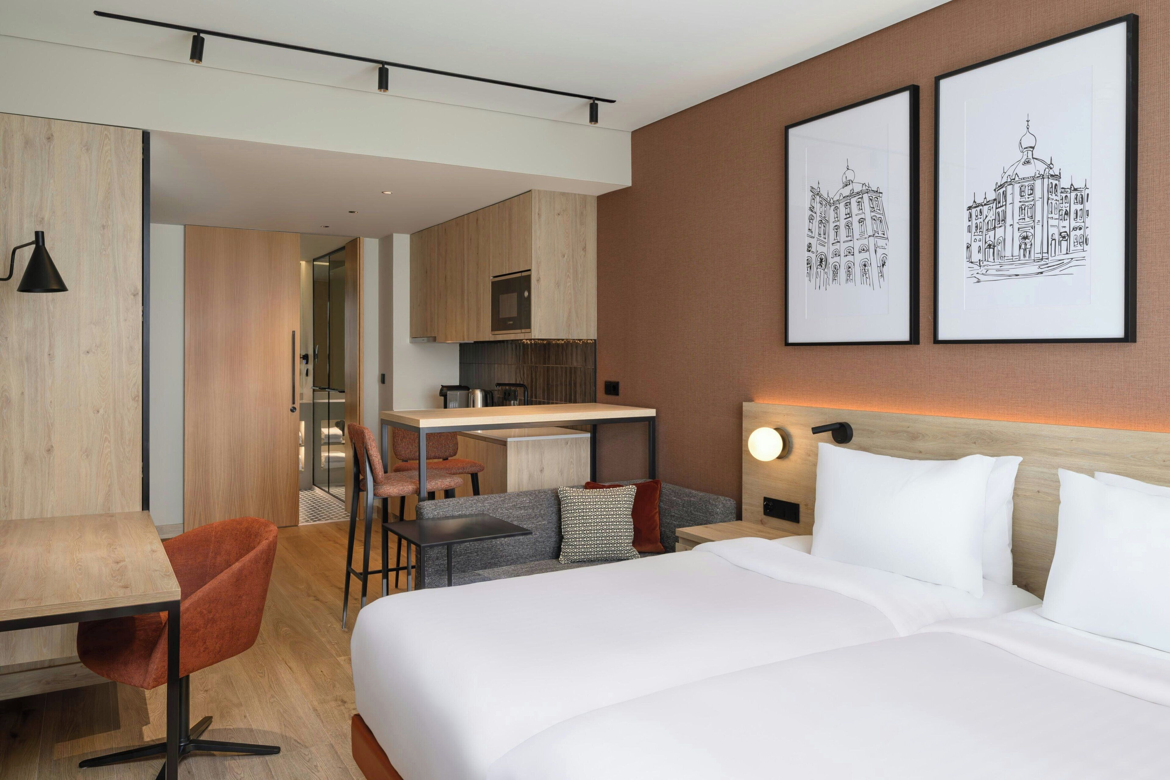 A modern hotel room with a bed, a desk, and a sofa. There are two framed pictures on the wall.