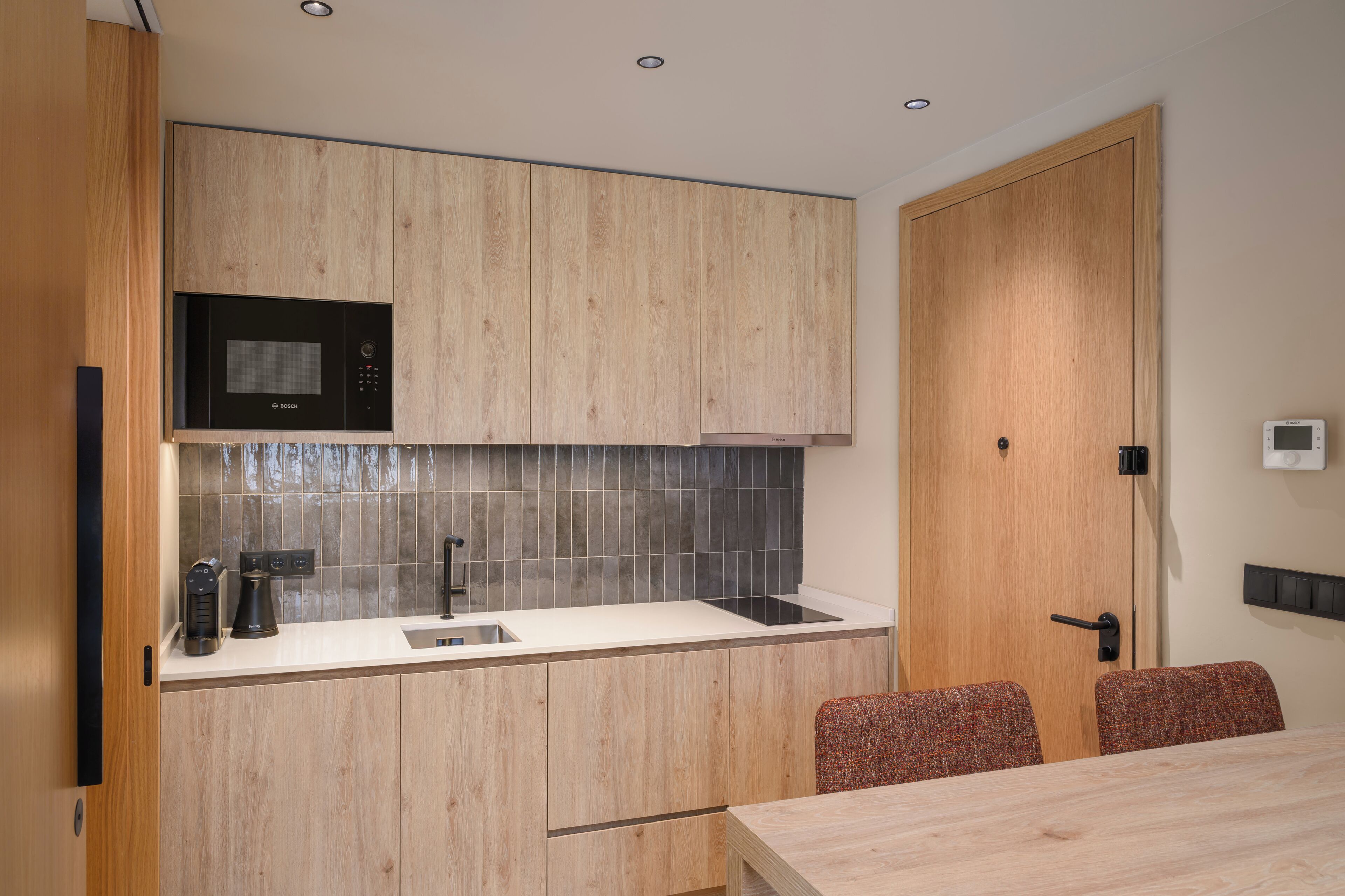A compact kitchen with wooden cabinetry, a Bosch microwave, a coffee maker, and a sink.