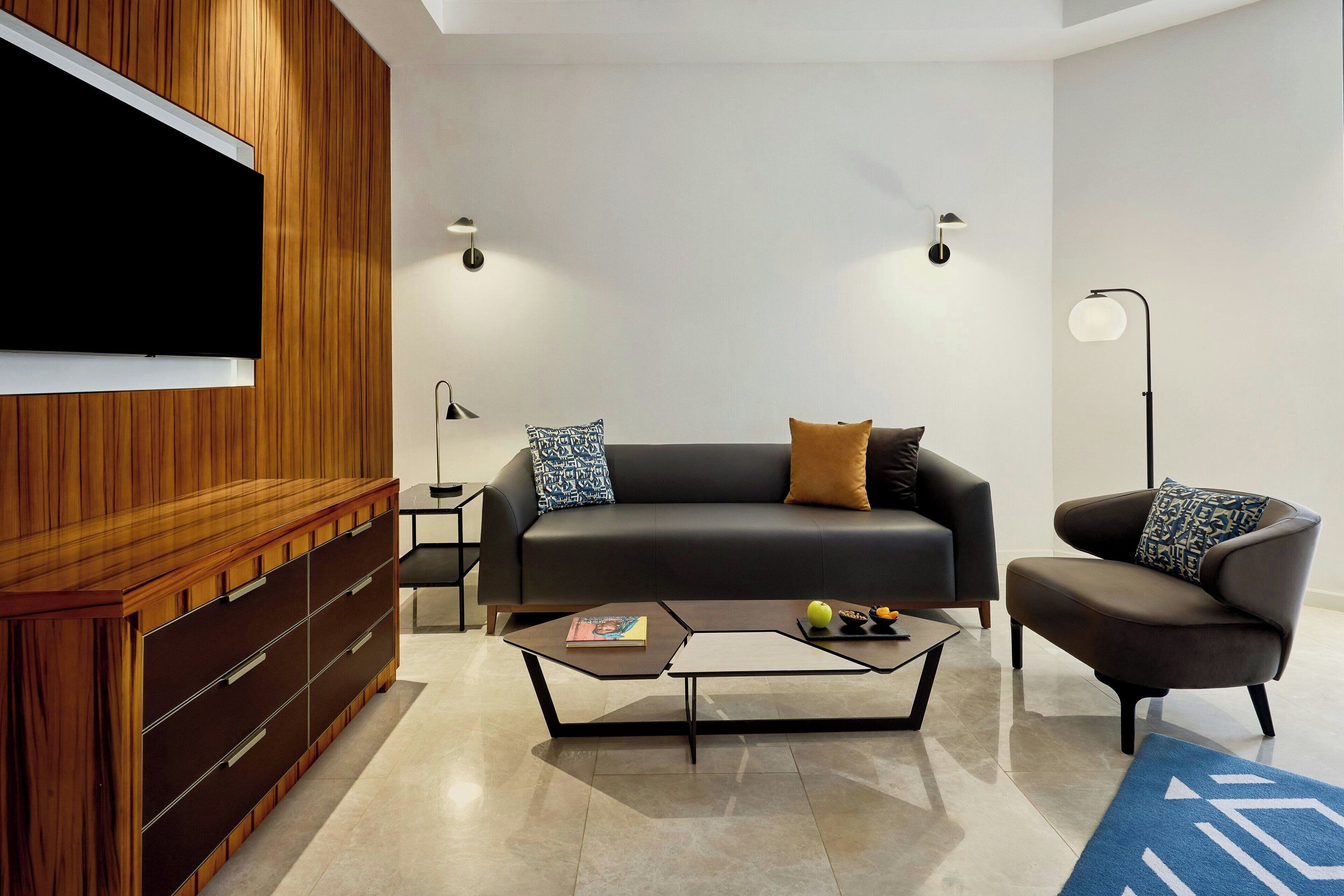 Una sala de estar moderna con un sofá, un sillón, una mesa de centro, un televisor y un aparador de madera.