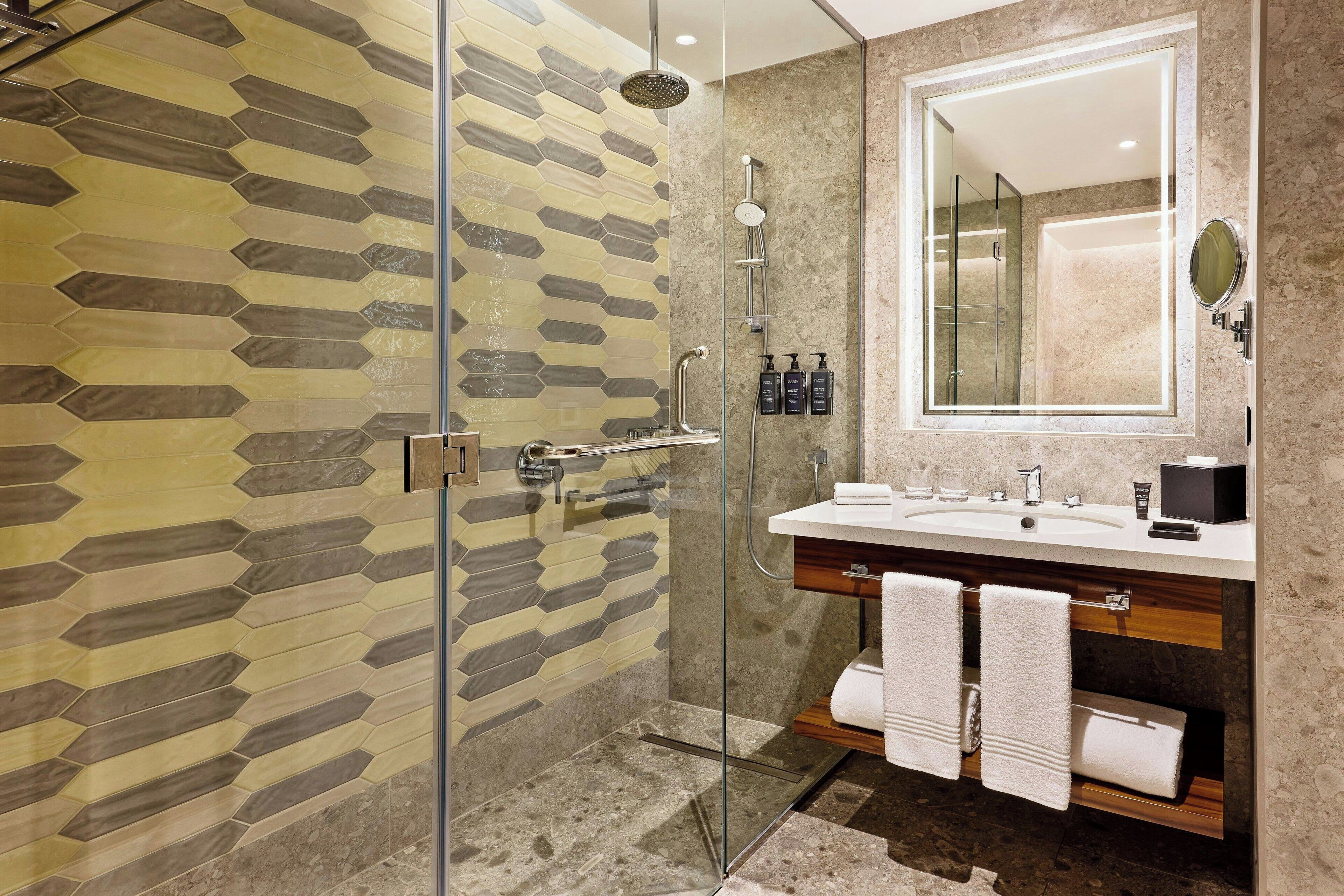 A modern bathroom with a glass shower enclosure, a large mirror, and a vanity with a sink and towel rack.