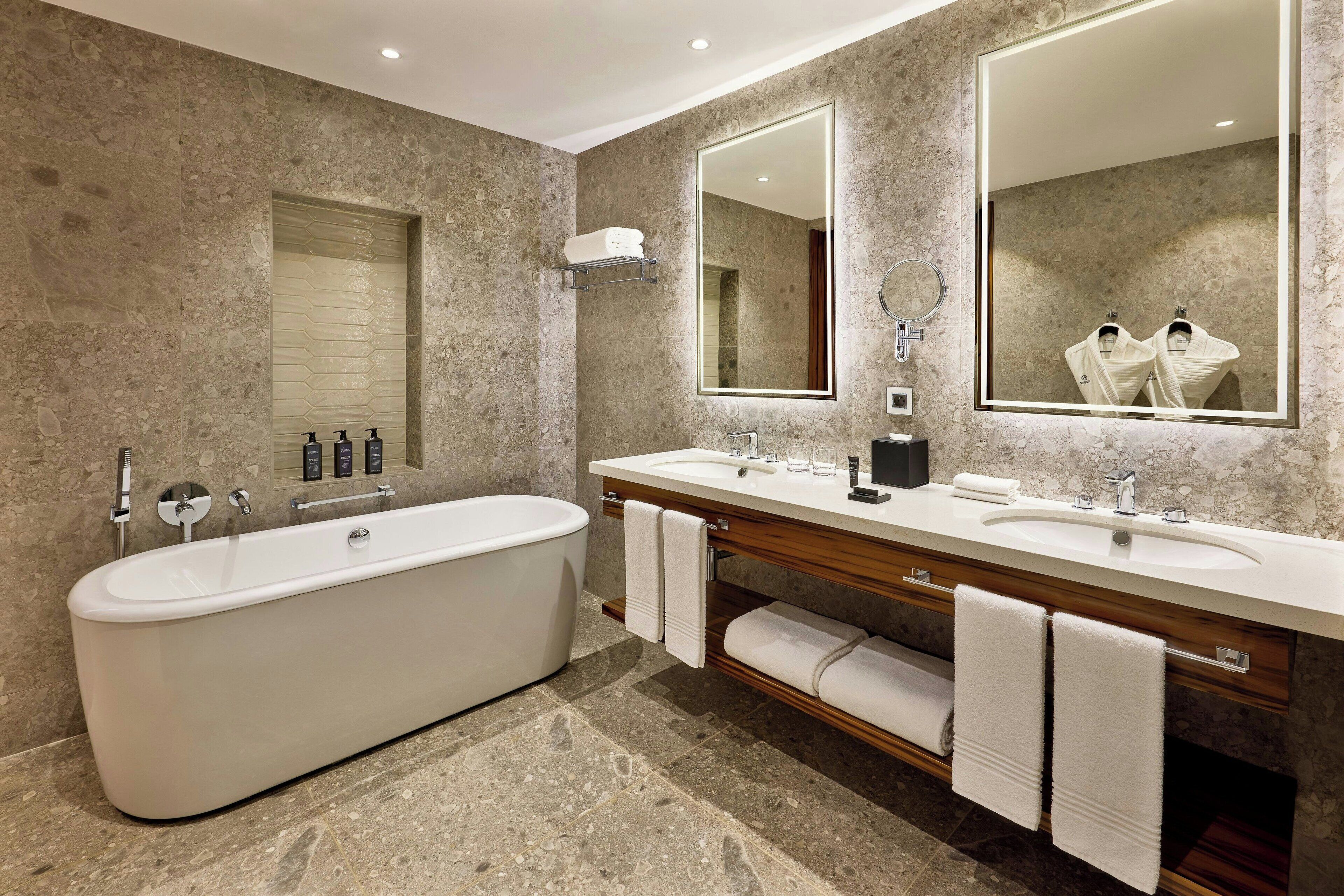 A modern bathroom with a freestanding bathtub, two sinks, and large mirrors.