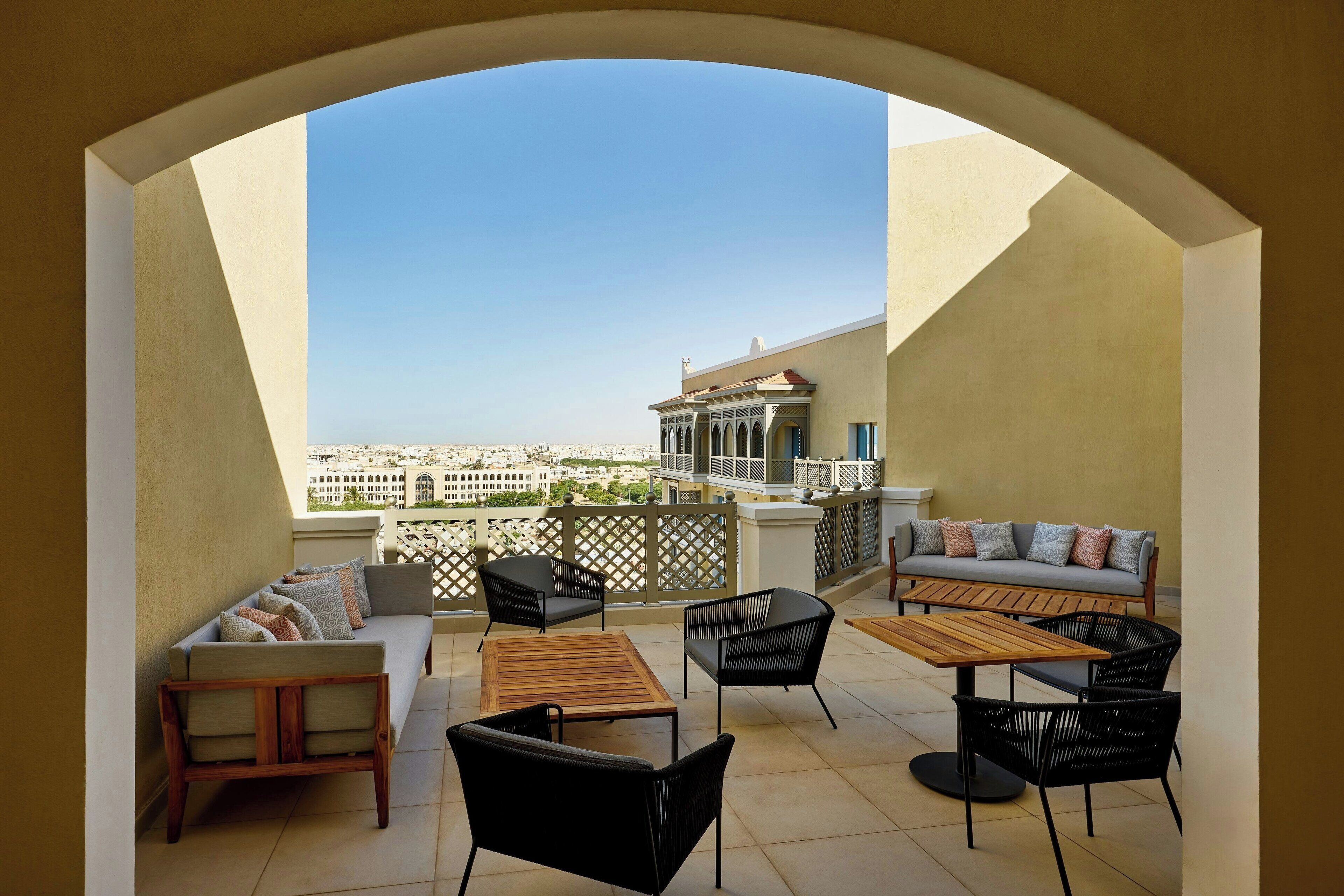 A balcony with a sofa, chairs, and a table, overlooking a cityscape.