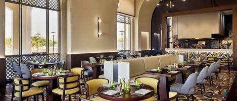A restaurant with round tables and chairs, a patterned carpet, and a view of the outdoors.