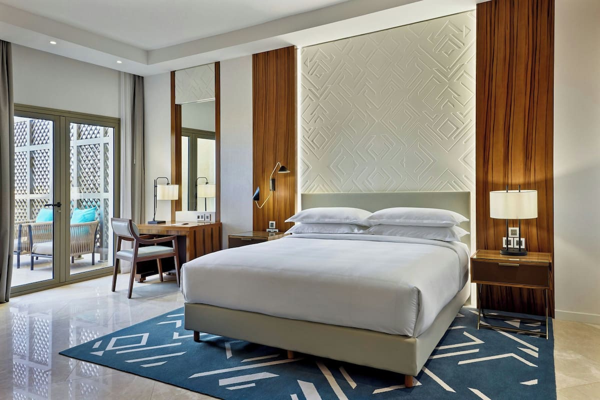 Habitación de hotel con una cama grande, un escritorio, una silla, una mesita de noche y vistas al exterior.