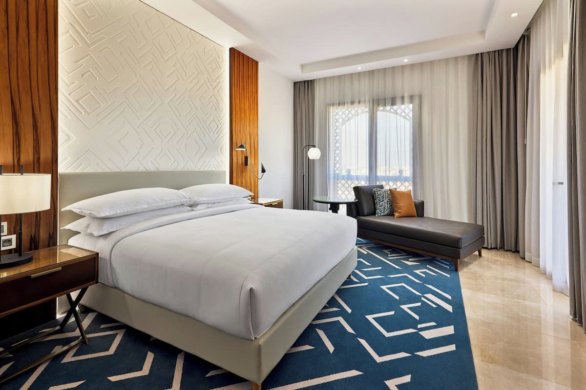 Una habitación de hotel moderna con una cama grande, un sofá, una mesita y vistas de la ciudad a través de amplios ventanales.