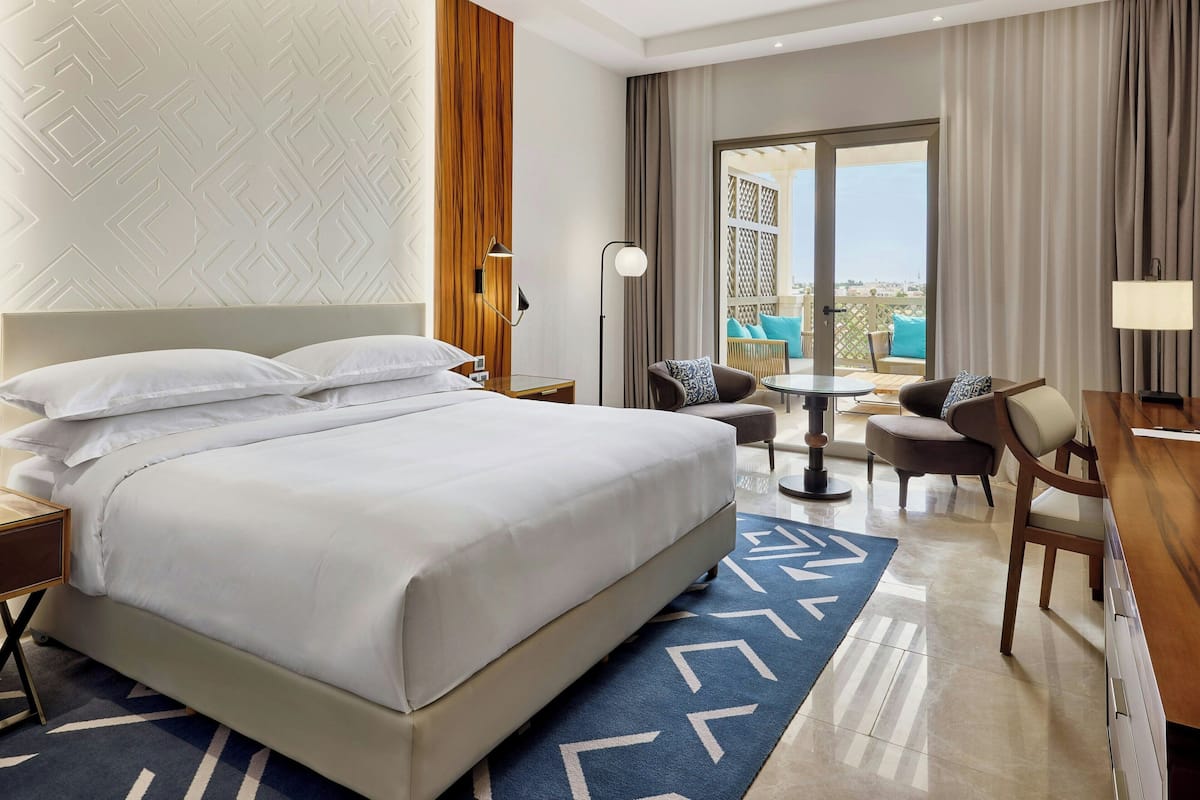 Habitación de hotel con una cama grande, un escritorio, una silla, una mesita y vistas al exterior.