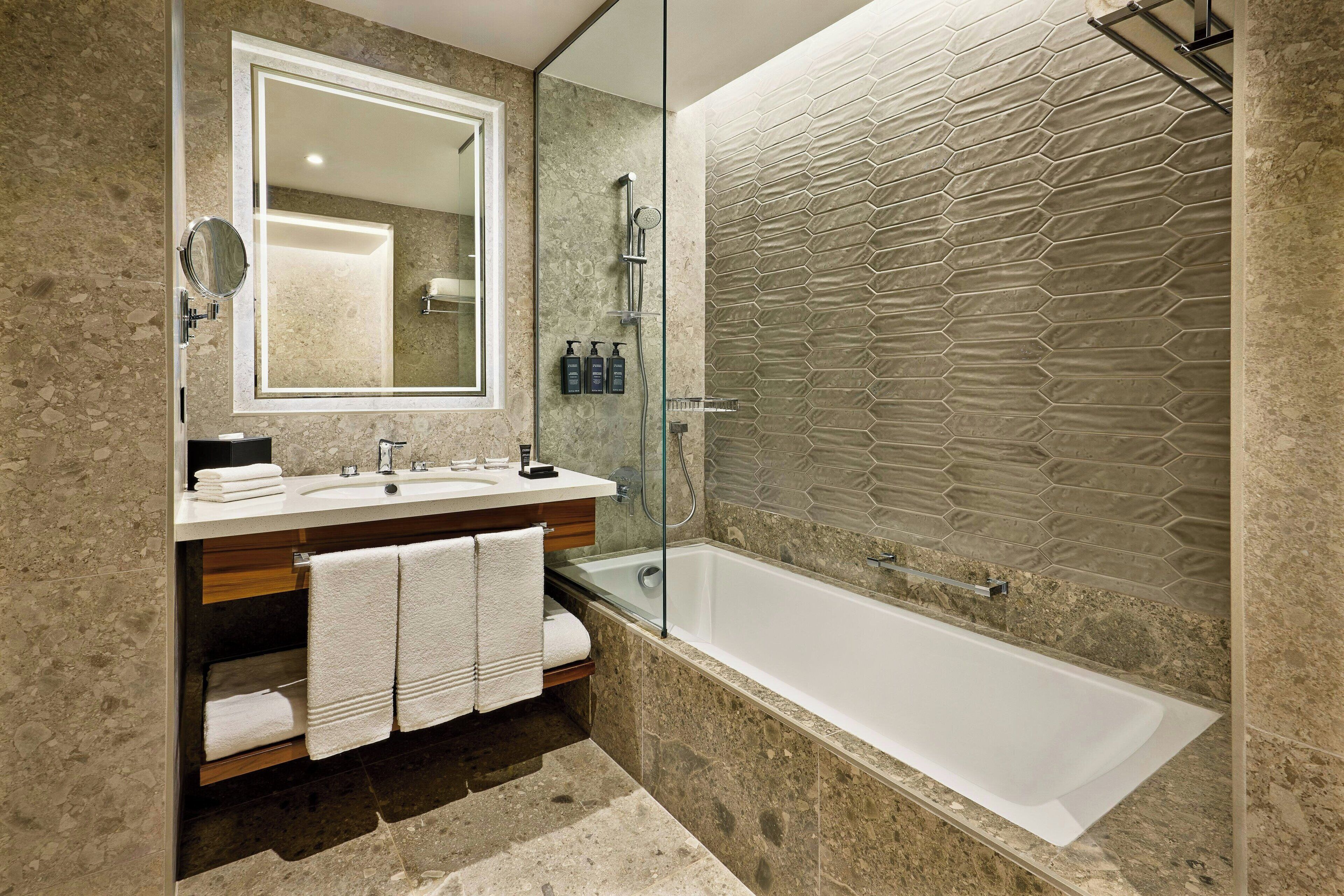 Un baño moderno con un espejo grande, dos lavamanos, ducha con mampara de vidrio y bañera.