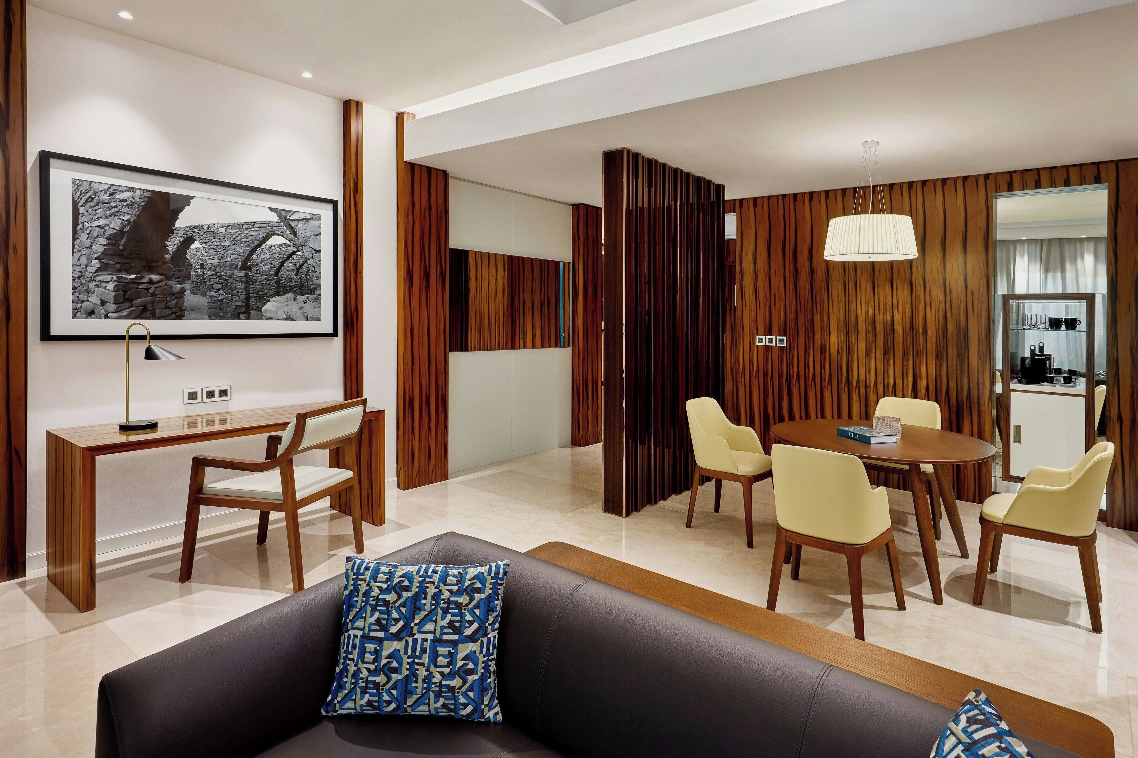 A modern living room with a black leather sofa, a wooden coffee table, and a dining area with a round table and chairs.
