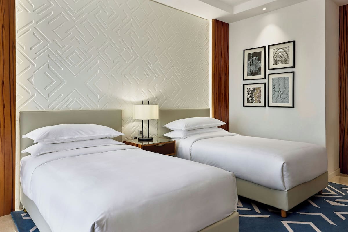 Una habitación de hotel con dos camas individuales, una mesita de noche con lámpara y una pared decorada con cuatro cuadros enmarcados.