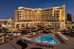A large hotel with multiple balconies, a swimming pool, and outdoor seating areas.