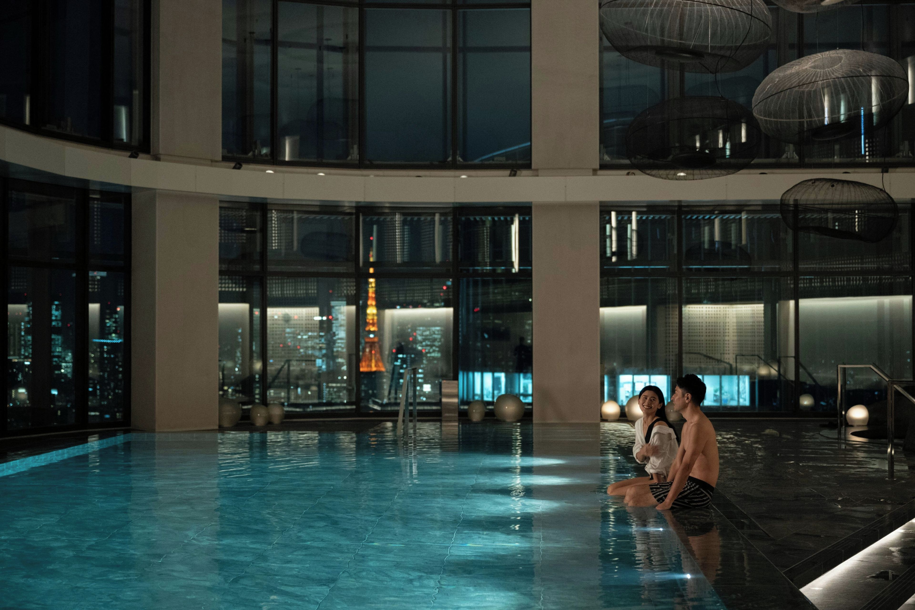 A spacious indoor swimming pool with a cityscape view through large windows.