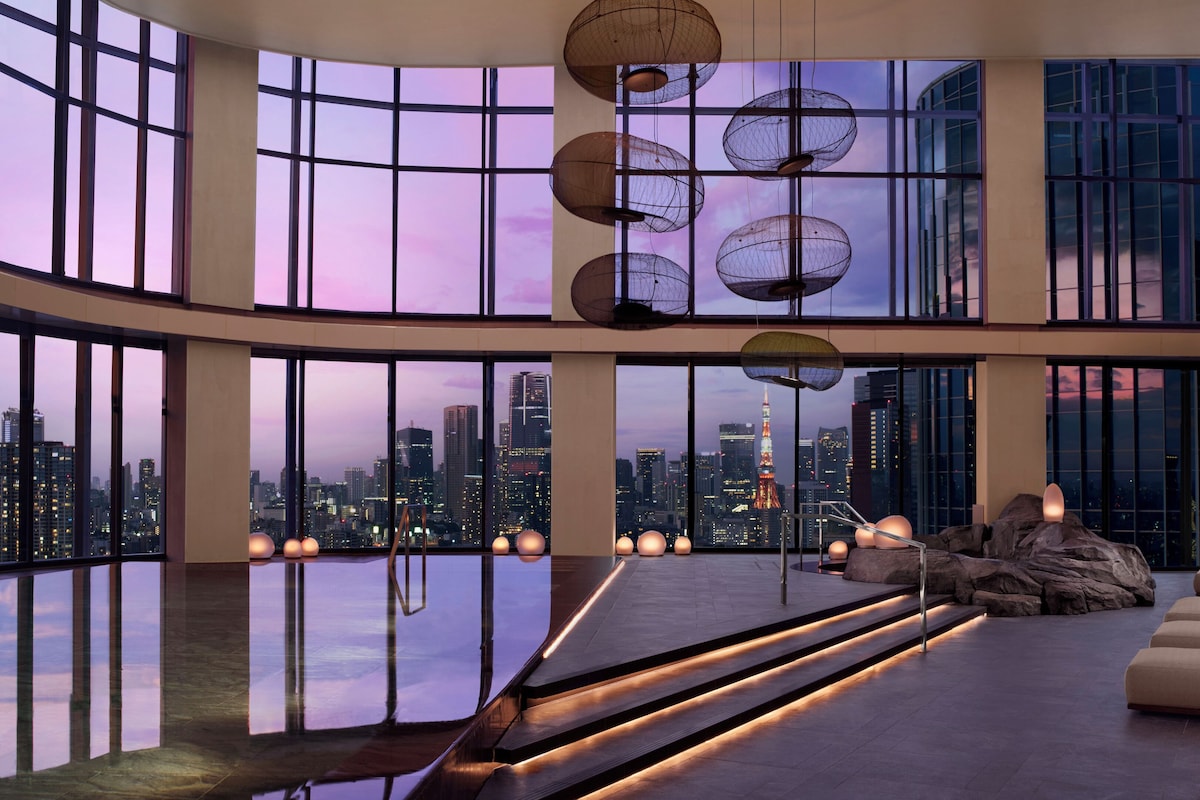 A spacious lobby with a reflective floor, large windows offering city views, a seating area with sofas, and a staircase with integrated lighting.