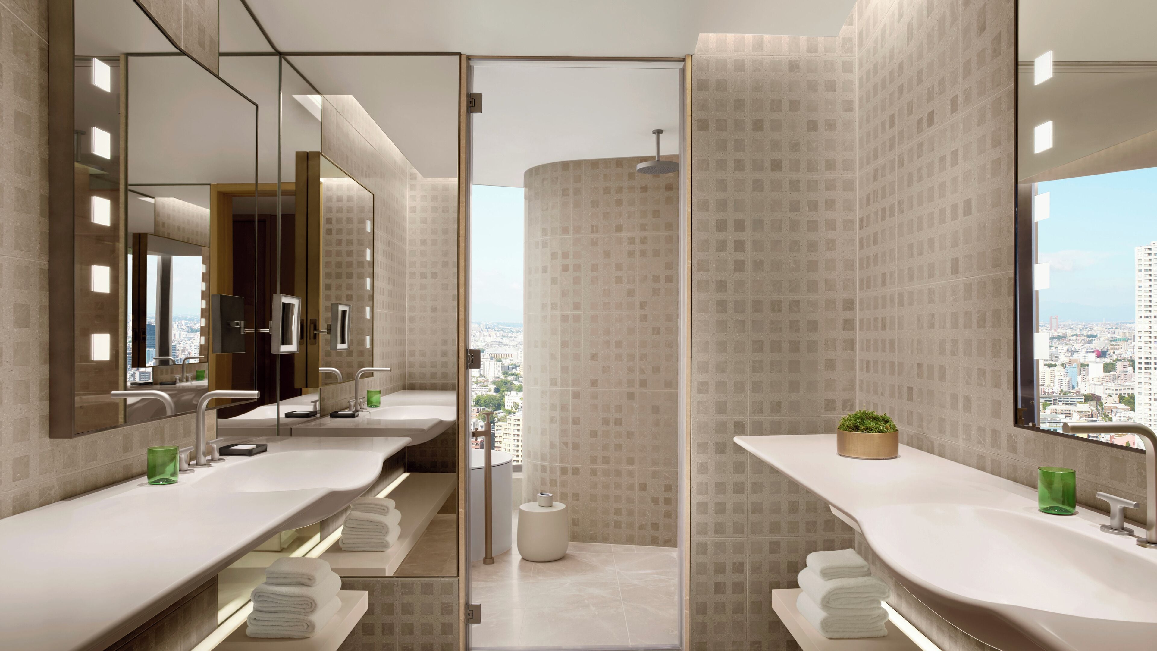 A modern bathroom with dual sinks, large mirrors, and a view of the city.
