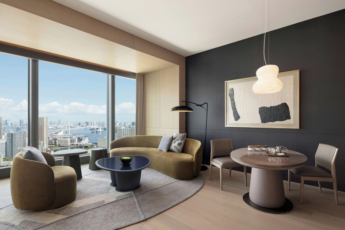 A modern living room with a city view, a round dining table, and a large abstract painting.