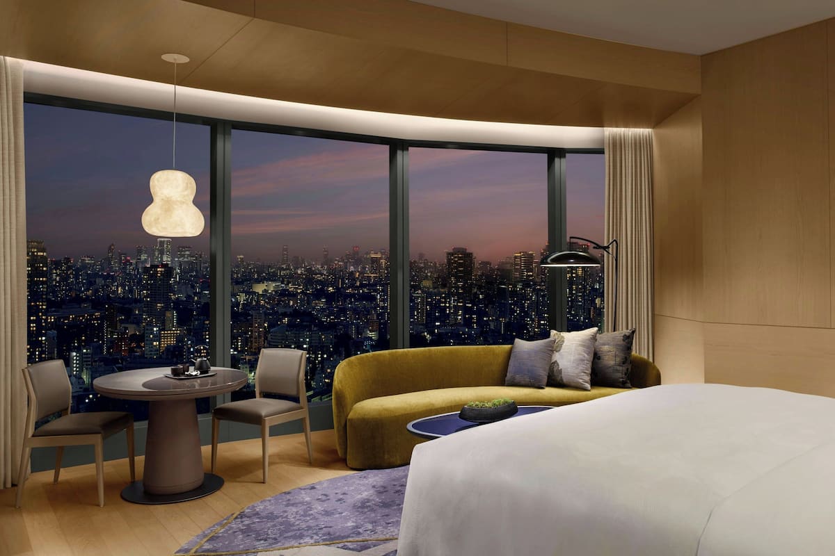 A modern hotel room with a city view, a round dining table, a sofa, and a bed.