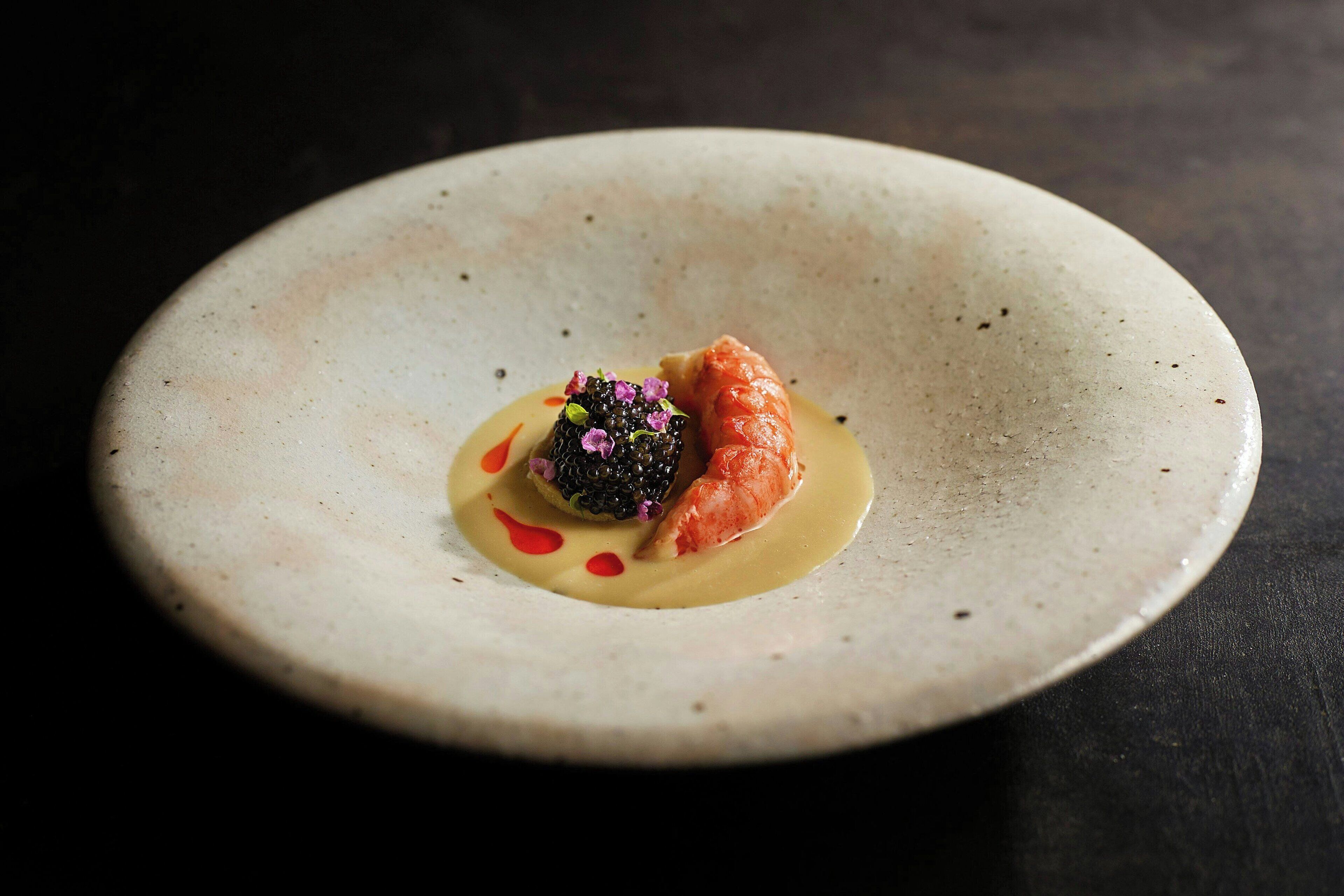 Une assiette contenant un dessert composé d’une compote de fruits rouges, d’un morceau de saumon et d’une sauce crémeuse.
