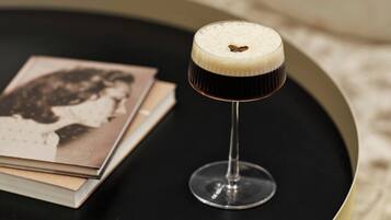 Un cocktail servi dans un verre à pied, décoré d’une garniture en forme de cœur, posé sur un plateau noir.