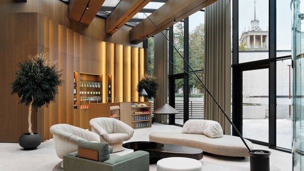 A modern interior with a seating area, a bookshelf, and a large window offering a view of a building.