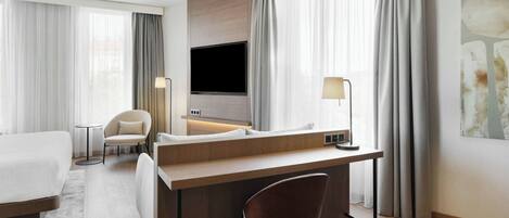 Habitación de hotel con cama, escritorio, silla, televisión y lámpara.